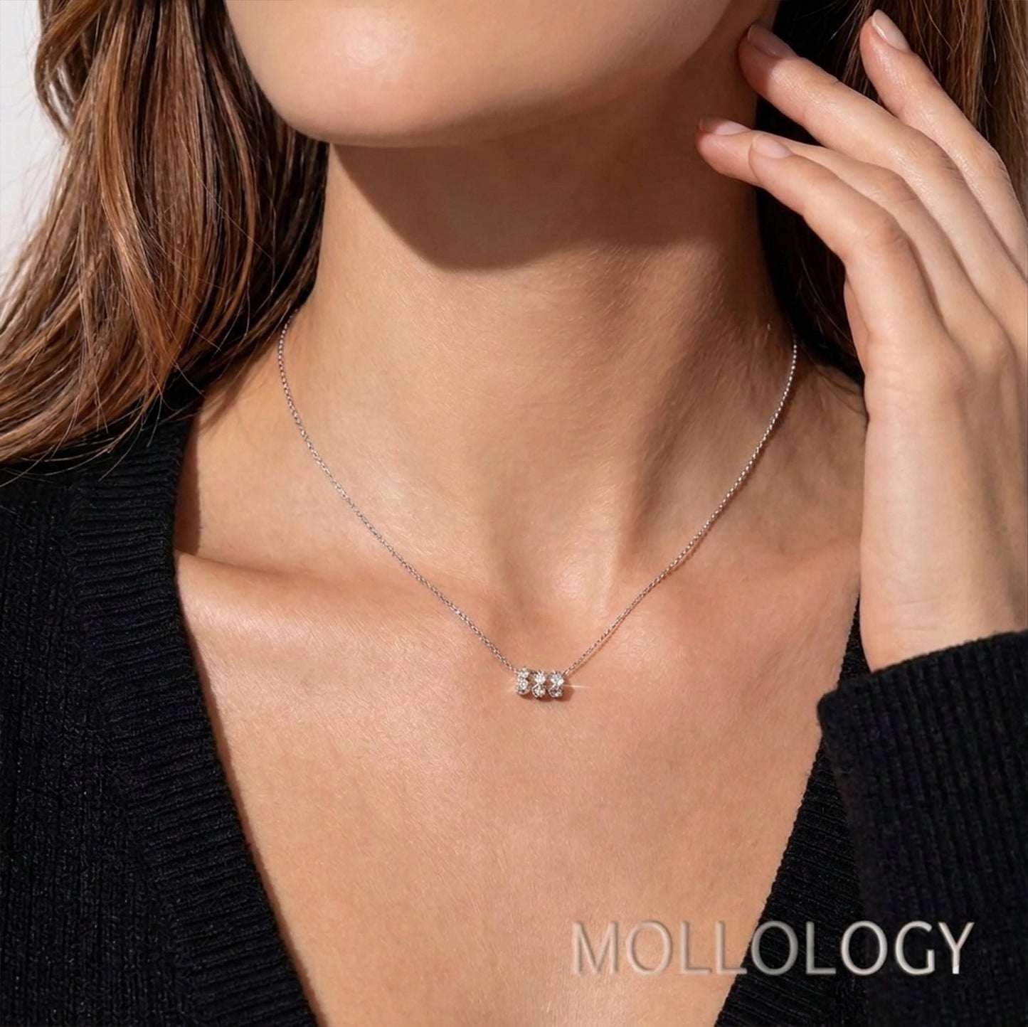 A close-up lifestyle shot of a model wearing a delicate silver chain necklace with a small three-stone cluster pendant. The model is wearing a black knit top, and the brand name 'MOLLOLOGY' is printed in white text in the bottom right corner.