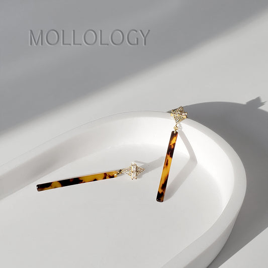 Tortoiseshell bar drop earrings with gold and baguette detail shown in a flat lay on a white background.