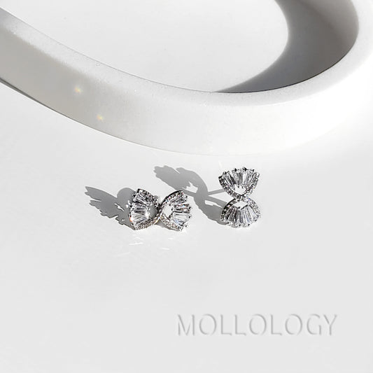 Pair of silver baguette bow stud earrings on white tray, minimalist diamond studs casting soft shadows
