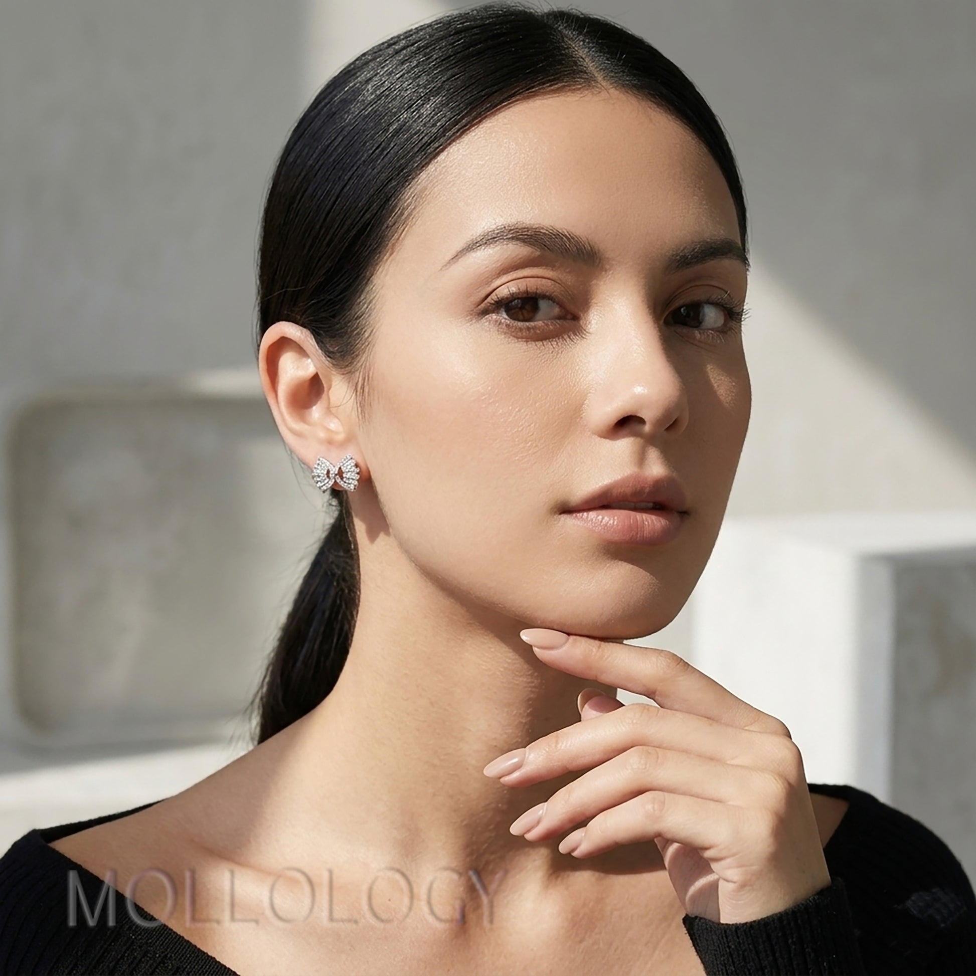 Model in black top wearing silver baguette bow stud earrings, closeup side view with natural light