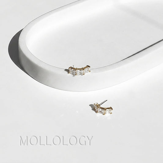 Pair of gold diamond earrings on a white surface, branded 'Mollogology'.