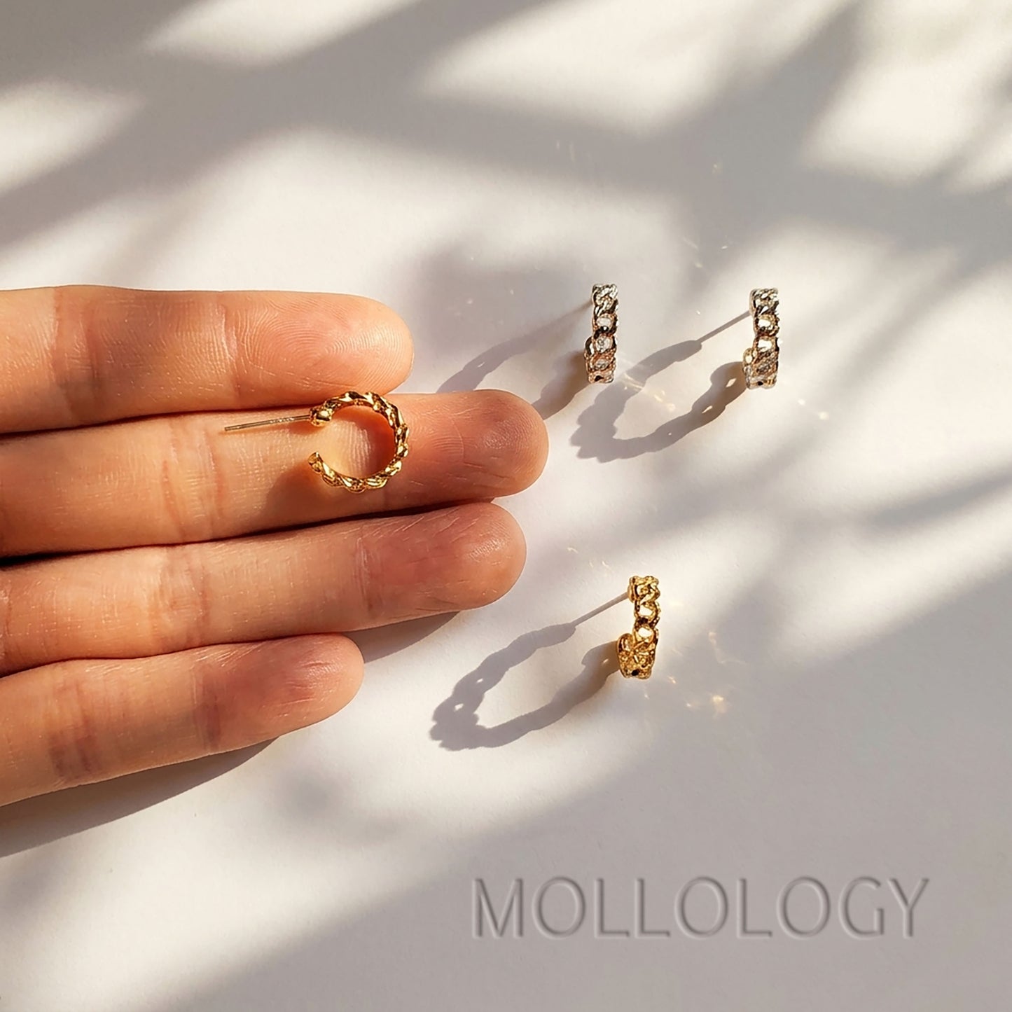 Gold chainlink huggie earring held between fingers with a close-up view of the textured hoop.