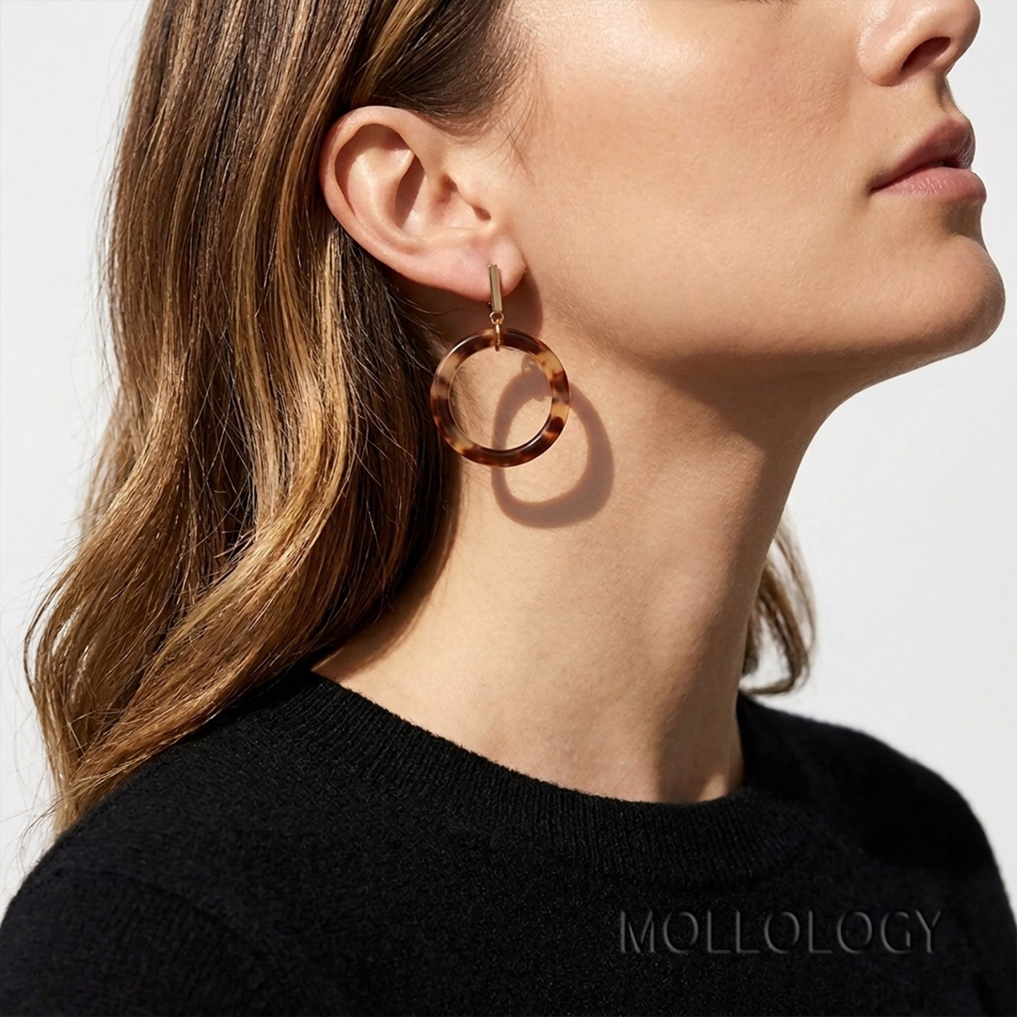 Side profile of woman wearing tortoiseshell acrylic circle dangle earrings with gold bar stud, styled with a black knit sweater