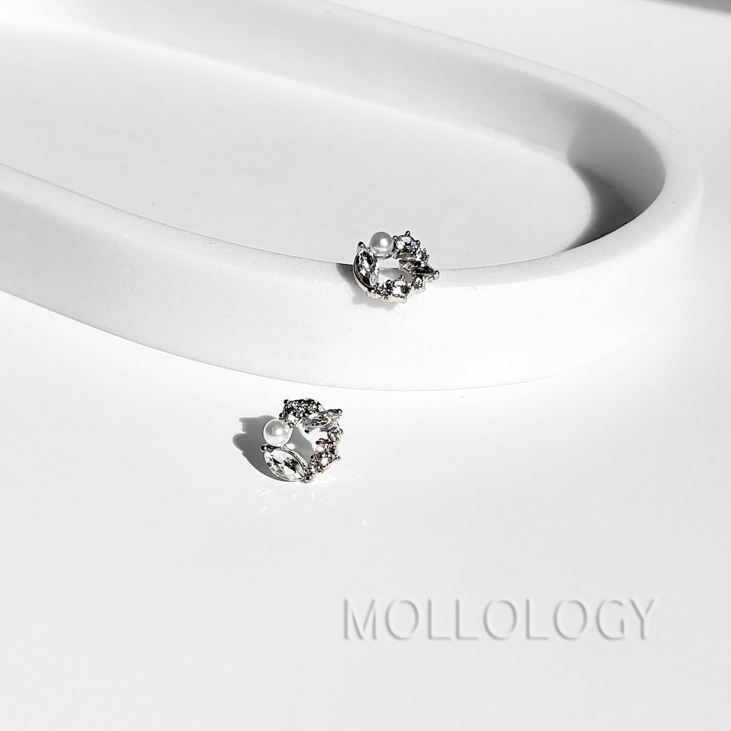 Pair of dainty pearl and cubic zirconia flower stud earrings displayed on a white curved tray.