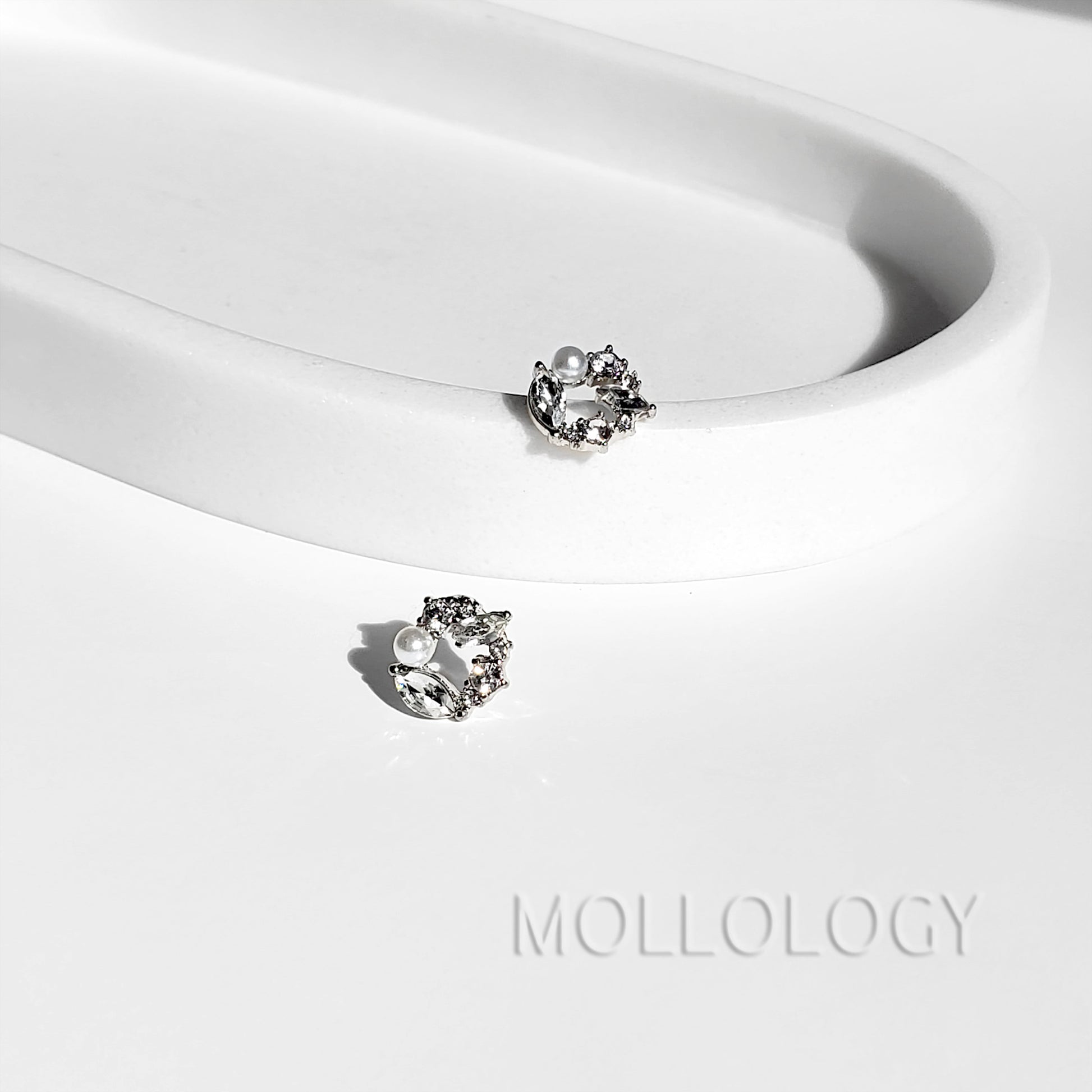 Pair of dainty pearl and cubic zirconia flower stud earrings displayed on a white curved tray.