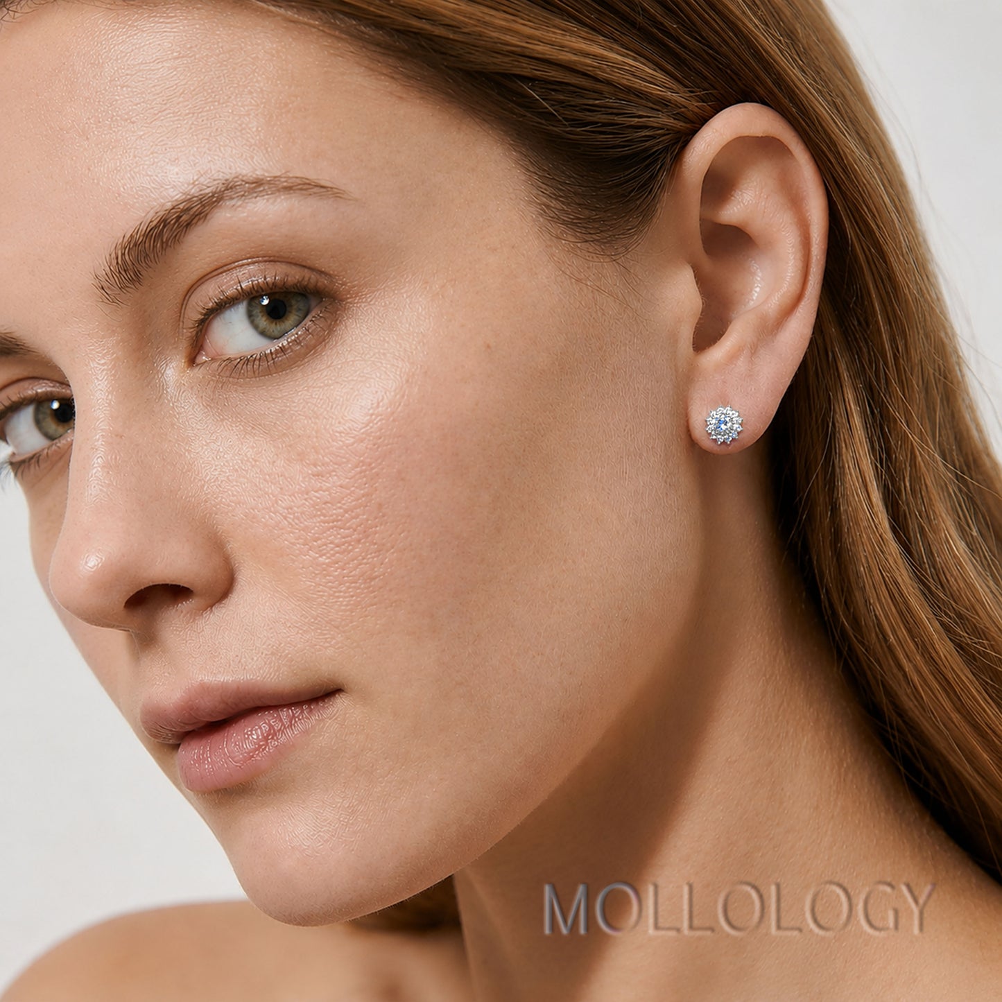 A close-up of a woman's ear wearing a small round stud earring with a clear gemstone in a silver-toned setting. The brand name MOLLOLOGY is visible as a watermark at the bottom right.