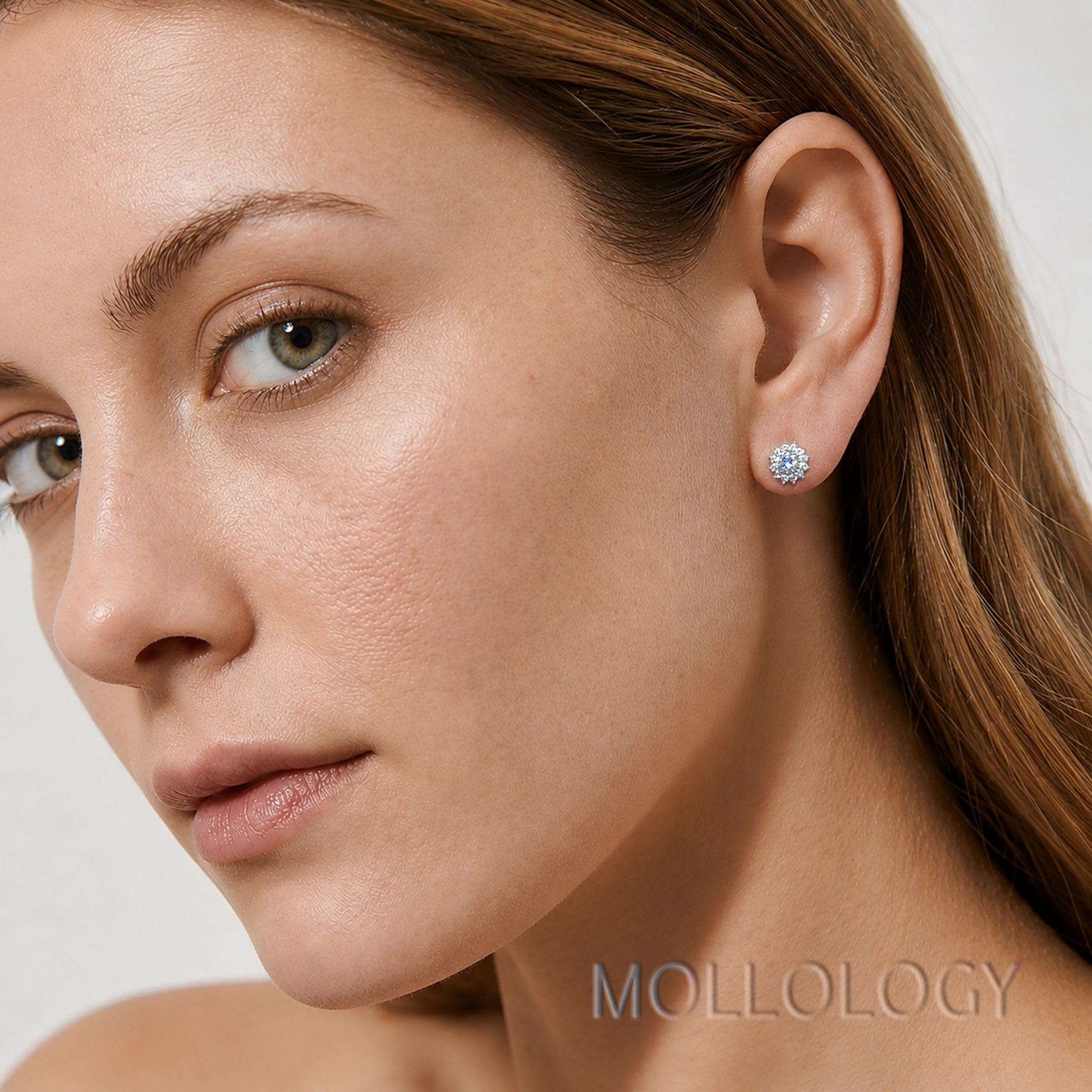 A close-up of a woman's ear wearing a small round stud earring with a clear gemstone in a silver-toned setting. The brand name MOLLOLOGY is visible as a watermark at the bottom right.