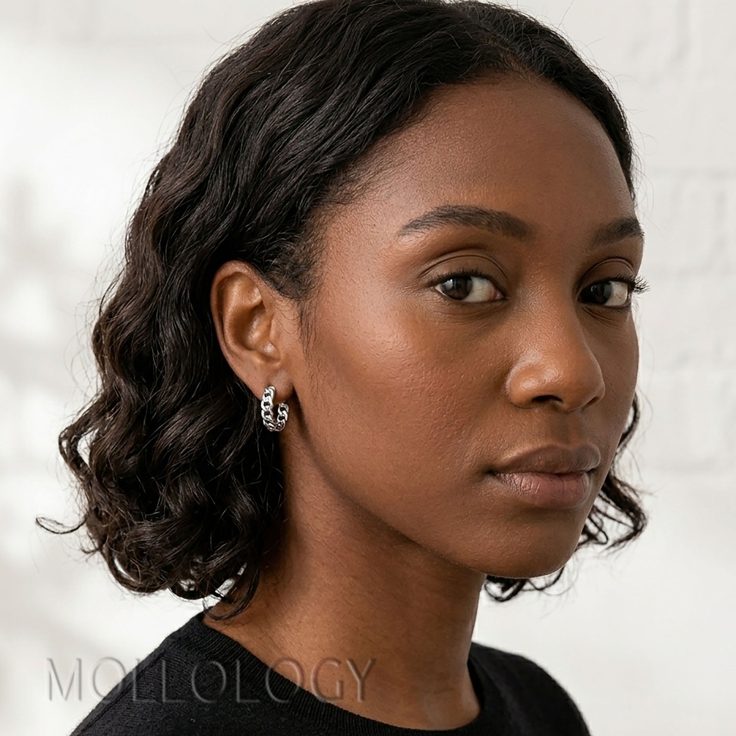 Model wearing small silver chainlink huggie hoop earrings.