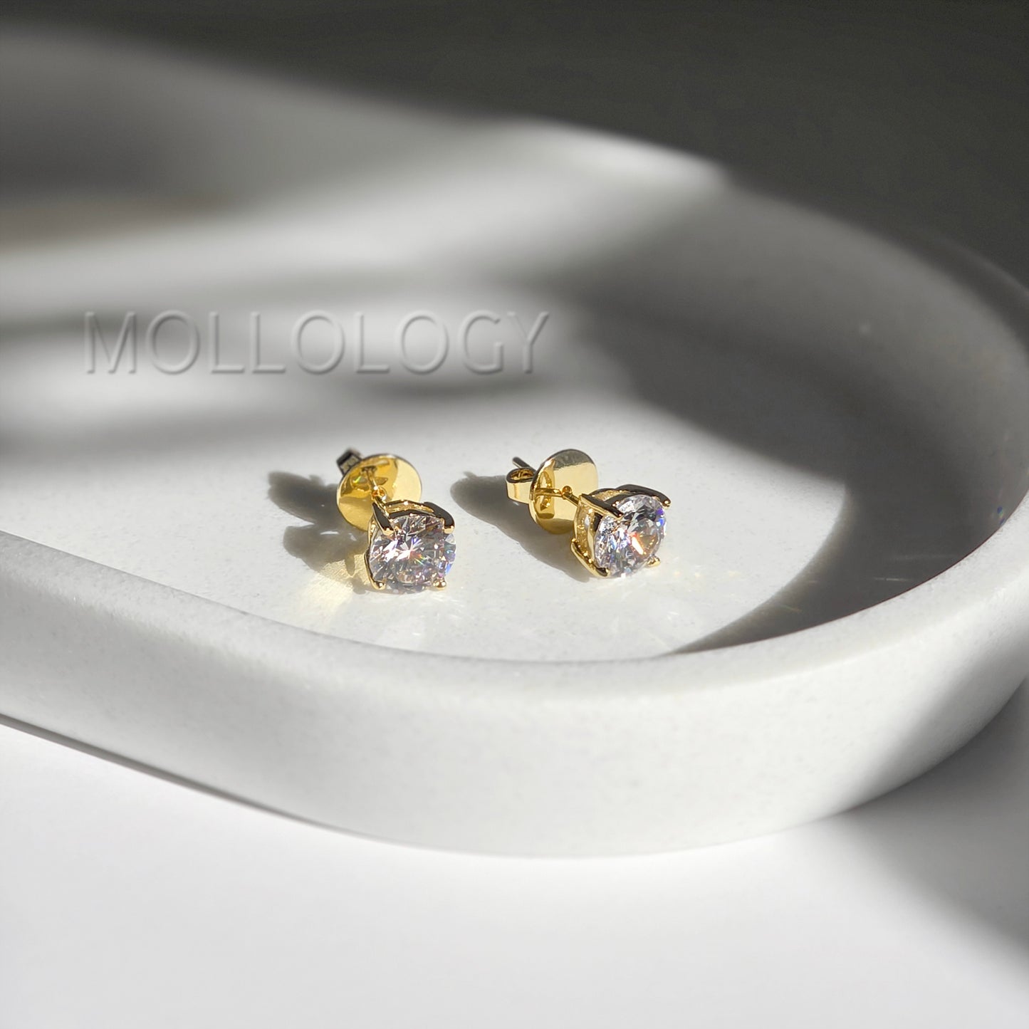 Gold round CZ solitaire stud earrings resting on white tray, classic minimalist diamond-style studs