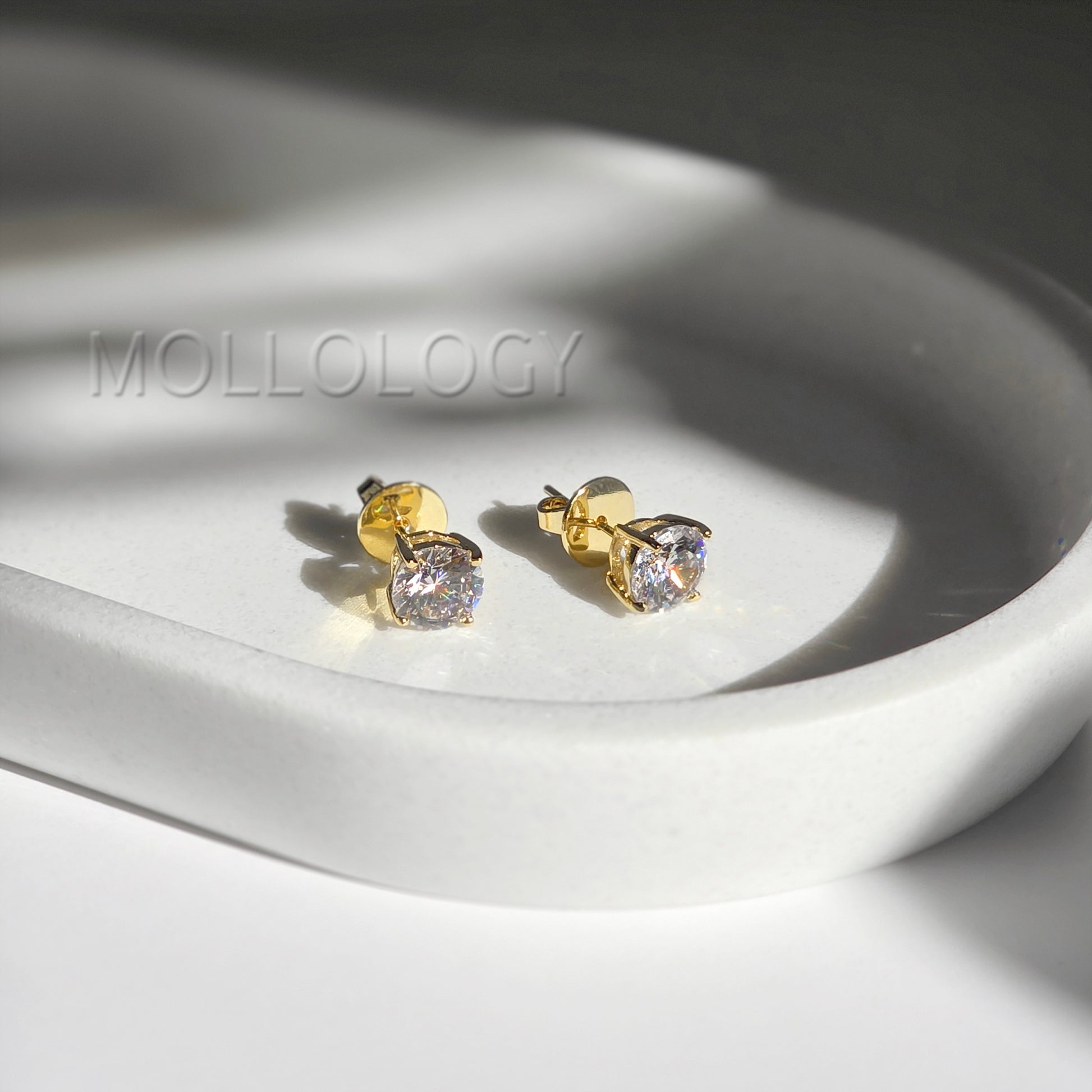 Gold round CZ solitaire stud earrings resting on white tray, classic minimalist diamond-style studs
