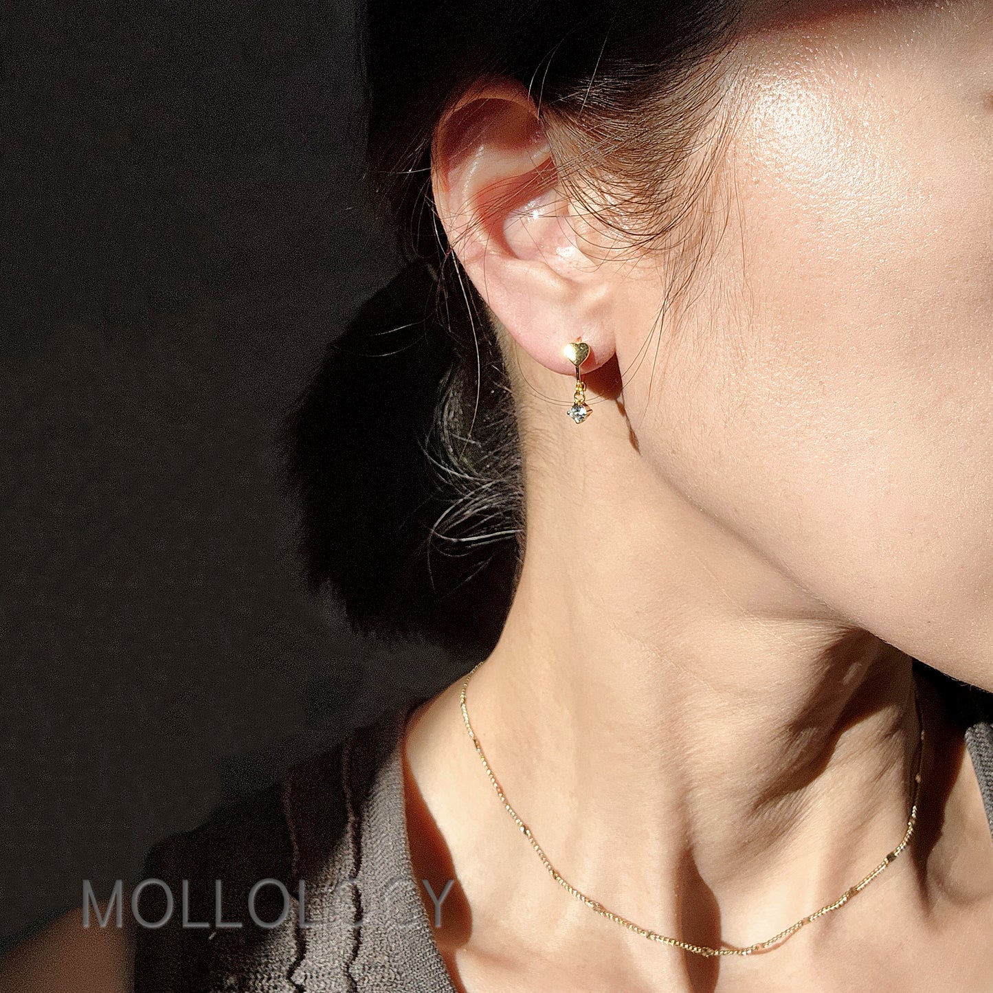 Model wearing tiny gold heart huggie hoop earrings.