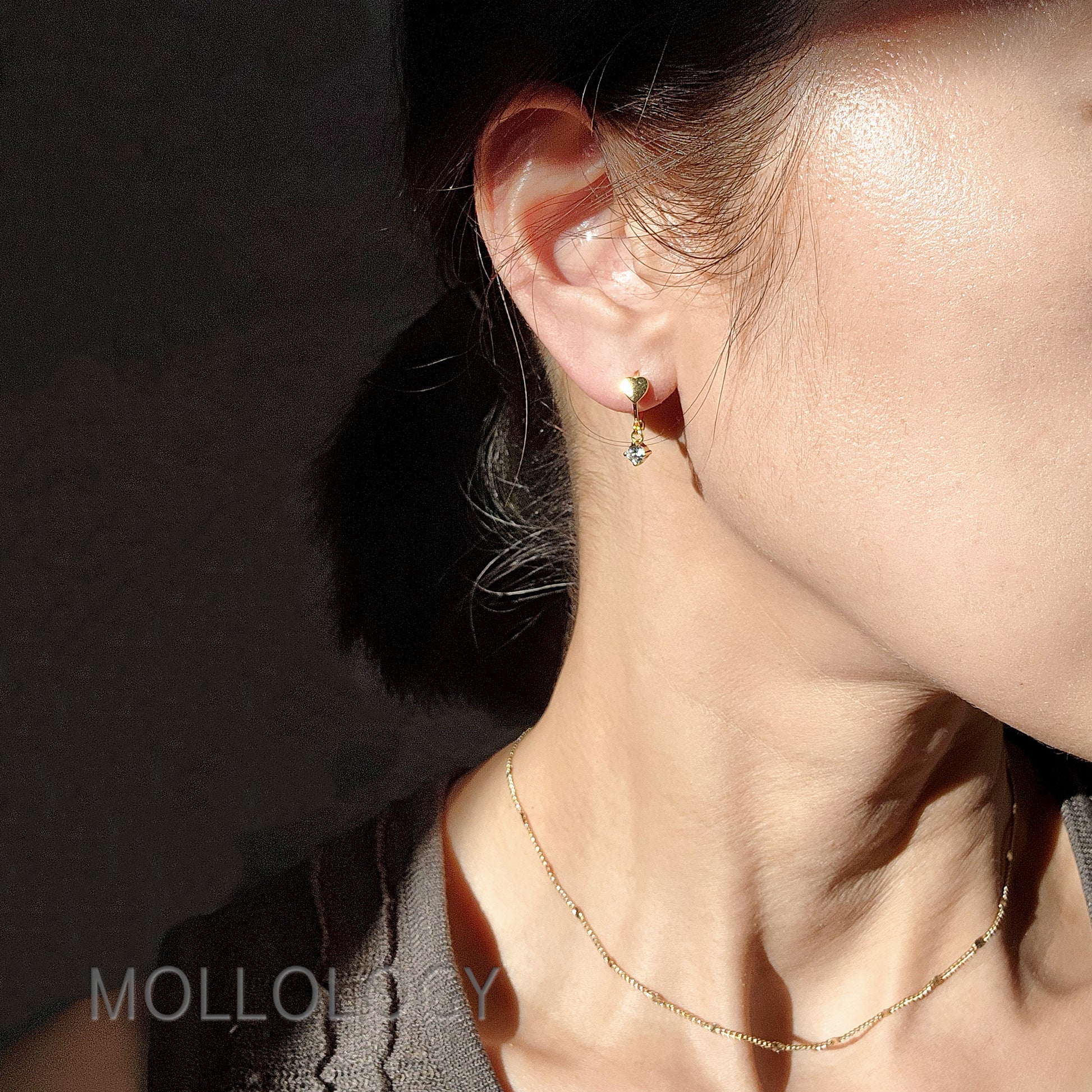 Model wearing tiny gold heart huggie hoop earrings.