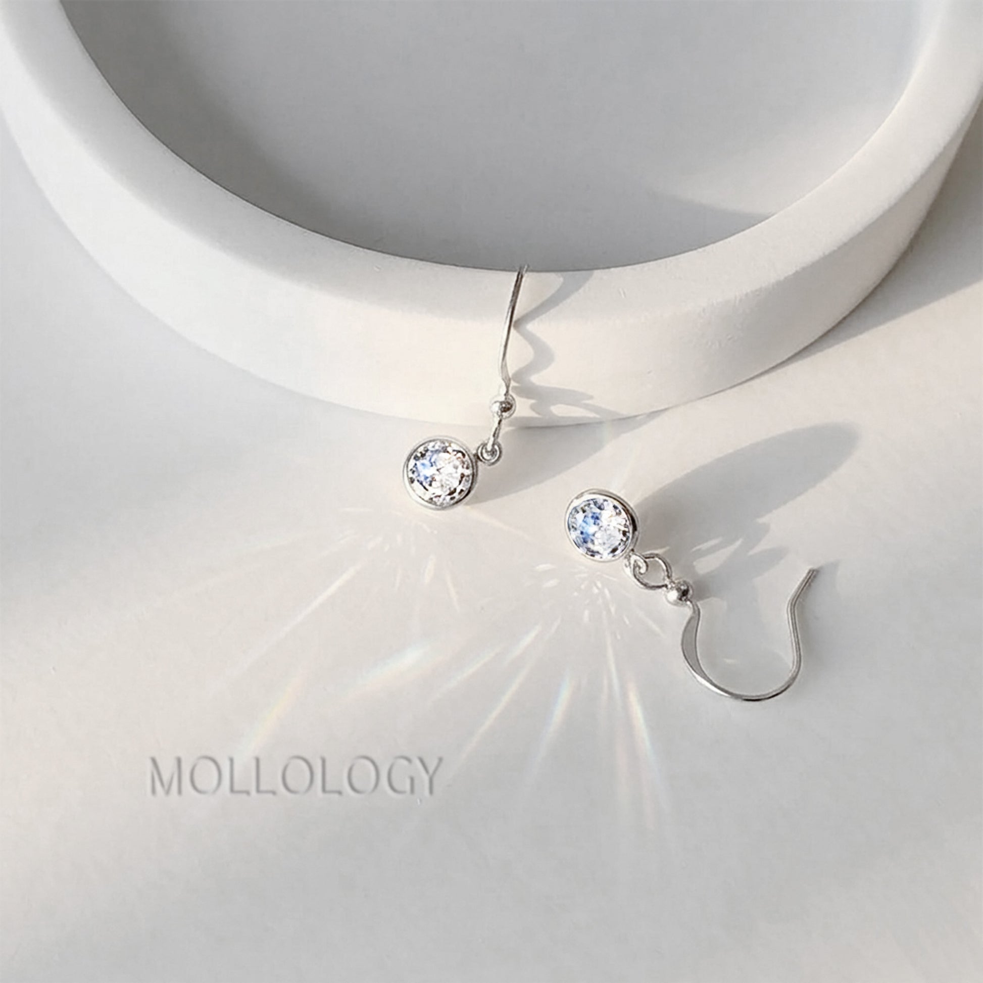 Silver bezel cubic zirconia drop earrings on white dish, minimalist dainty dangle studs with sparkle