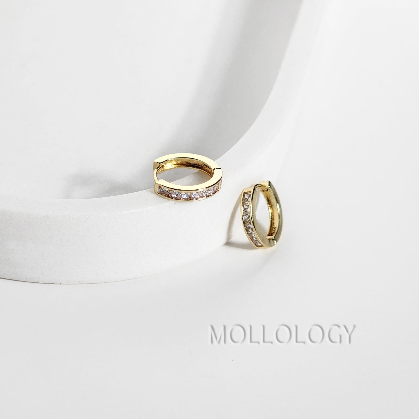 Gold hoop earrings with small diamonds on a white background, branded 'Mollog'.