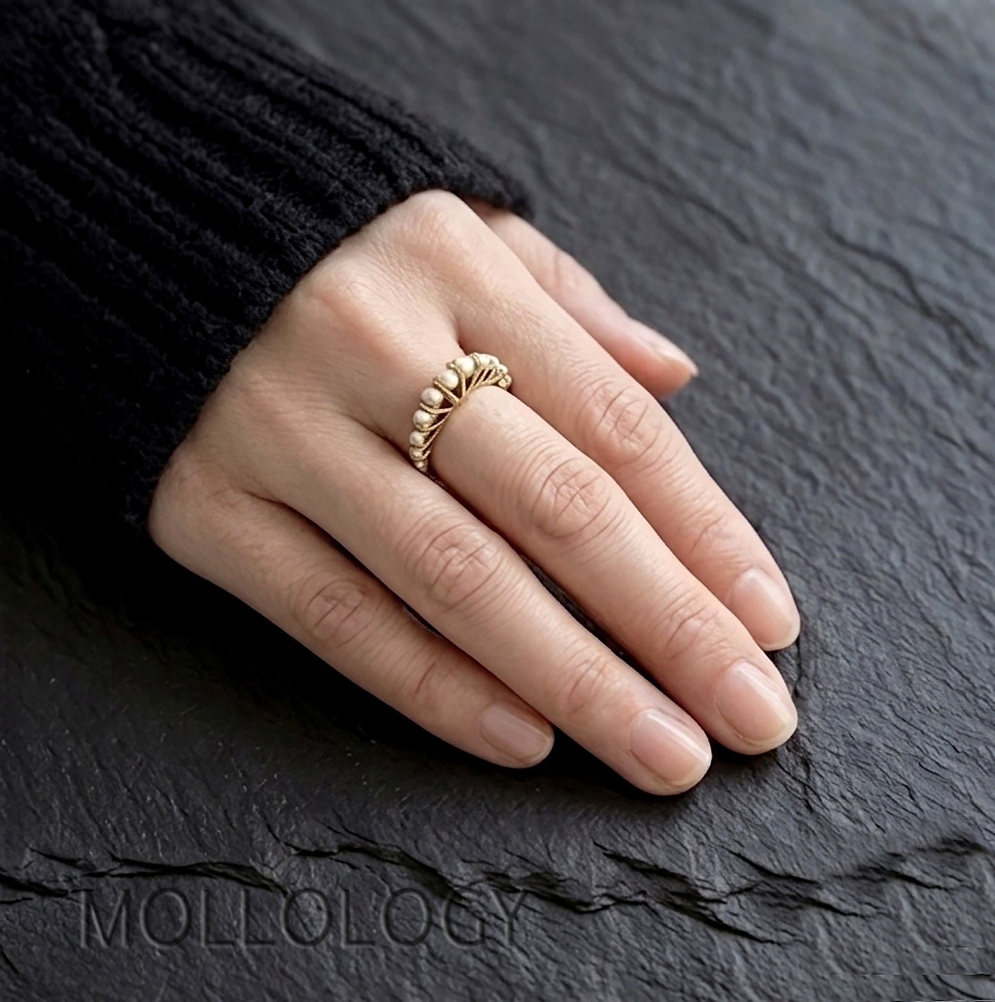 Gold arched pearl ring on model’s hand, 14k gold plated vintage fan style stacking ring on dark stone background