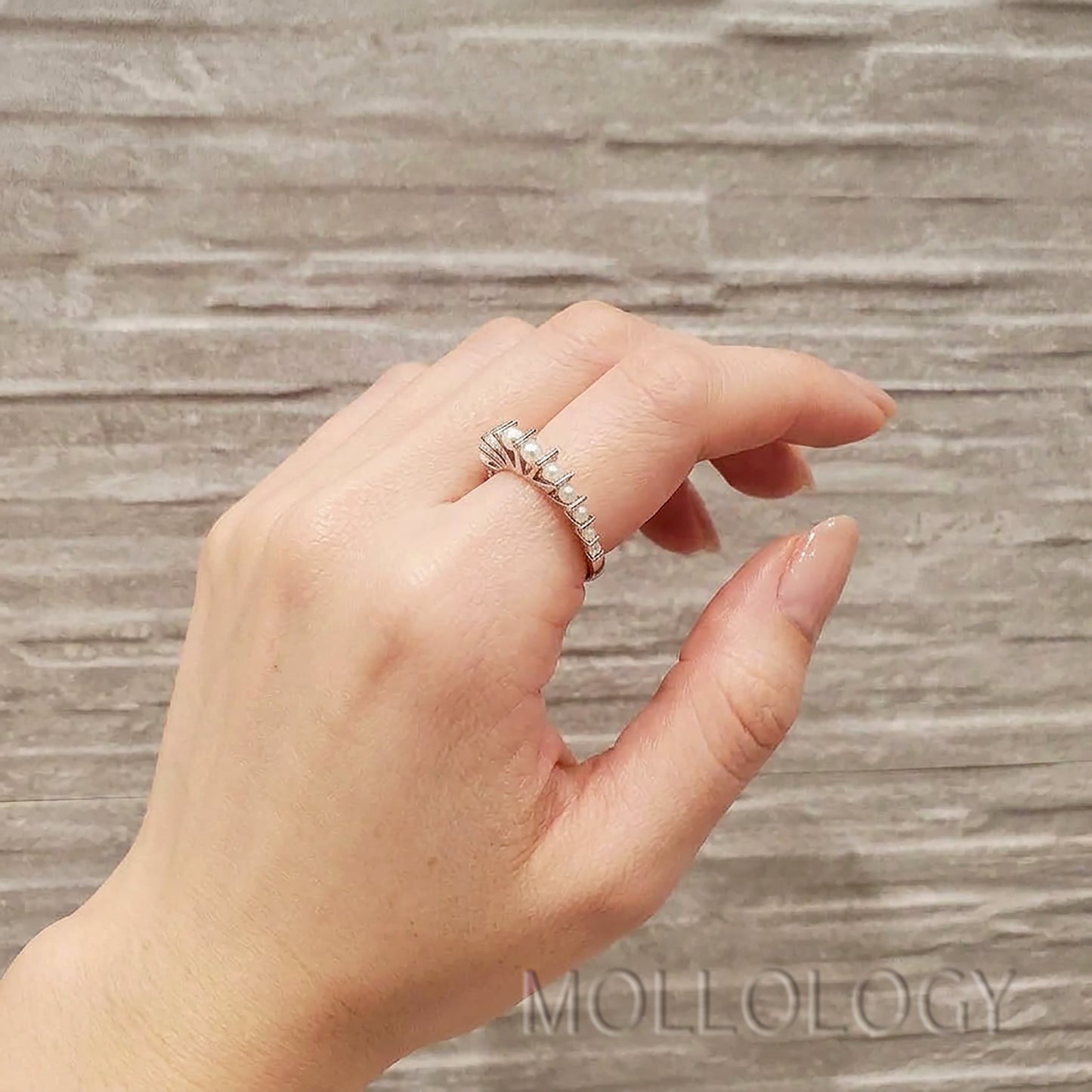 Silver pearl ring on smooth hand with light nude polish, side angle on textured stone background, dainty fan ring