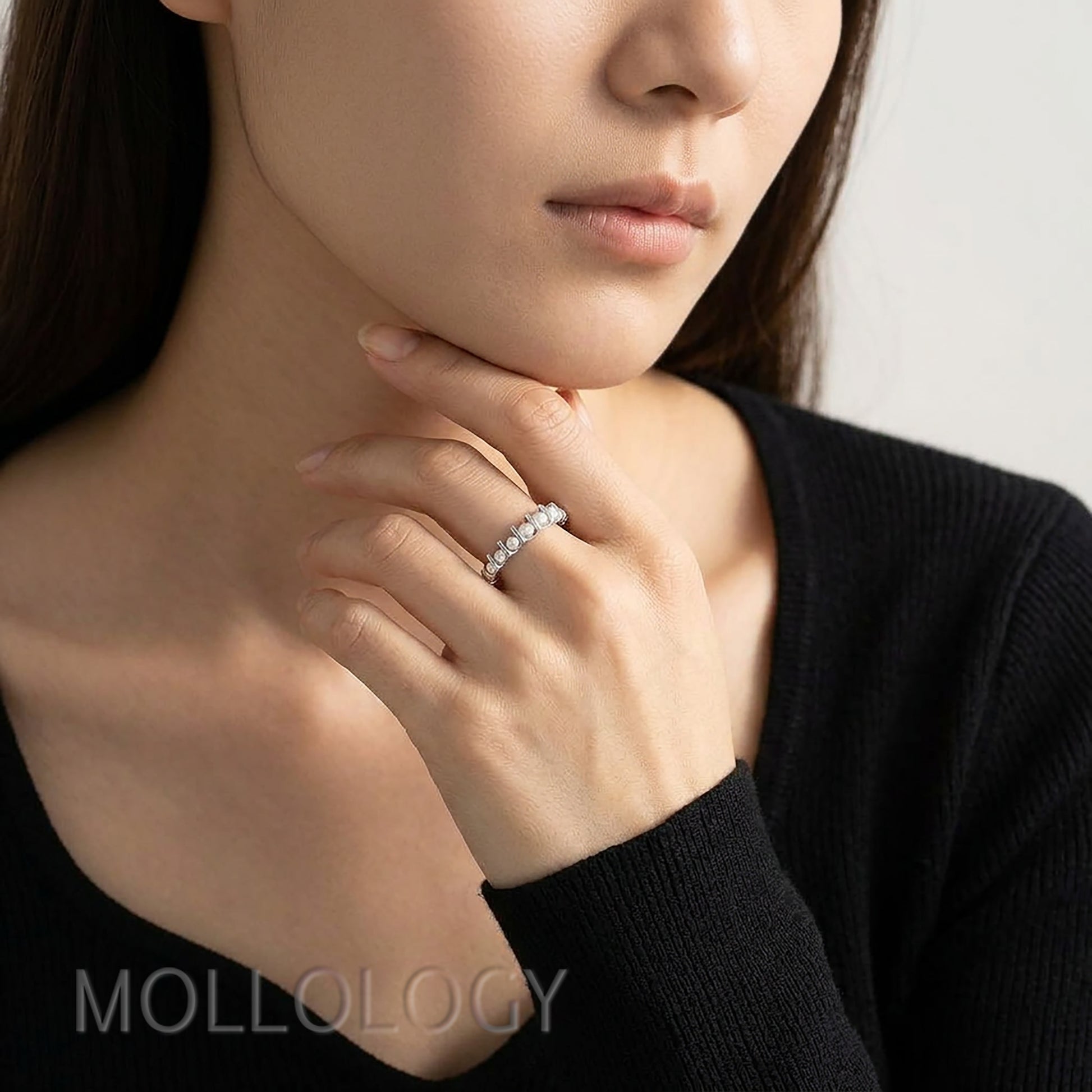 Model in black sweater wearing minimalist pearl ring near chin, cropped closeup, elegant dainty pearl jewelry gift