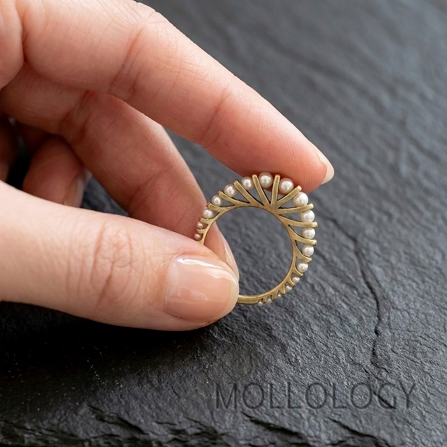 Gold arched pearl ring on model’s hand, 14k gold plated vintage fan style stacking ring on dark stone background