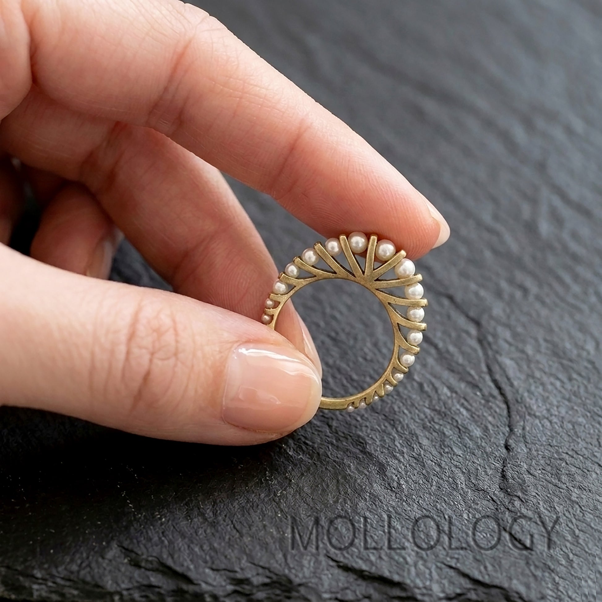 Gold arched pearl ring on model’s hand, 14k gold plated vintage fan style stacking ring on dark stone background
