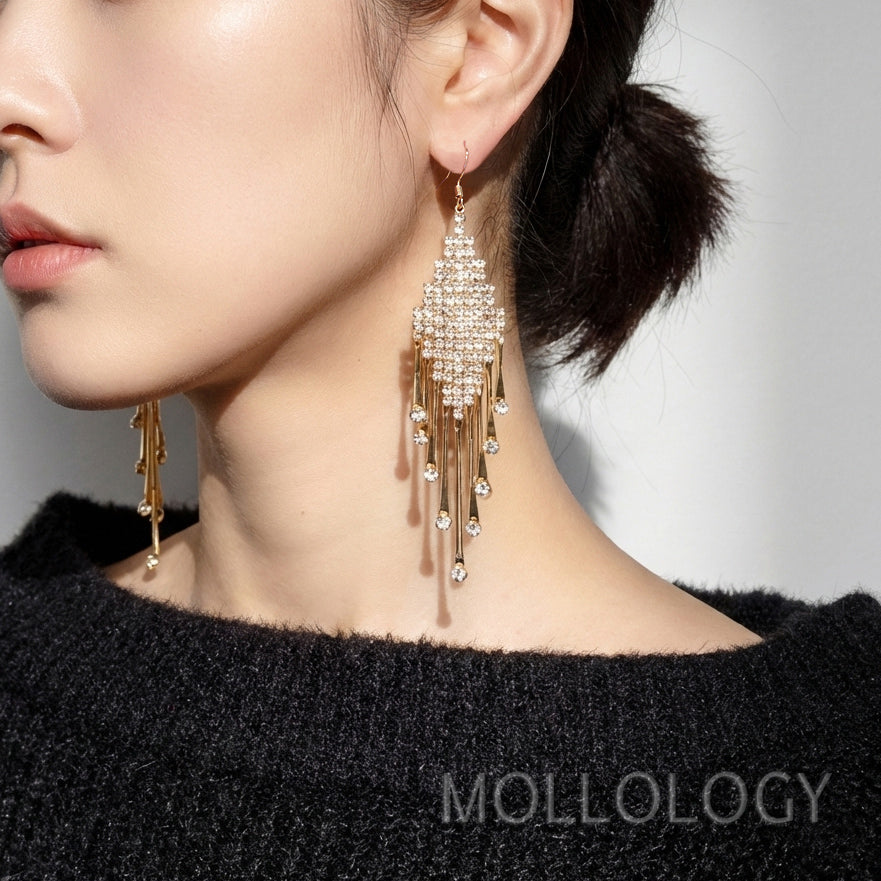 Close-up of a woman wearing gold earrings with tassels, branded 'Mollology'.