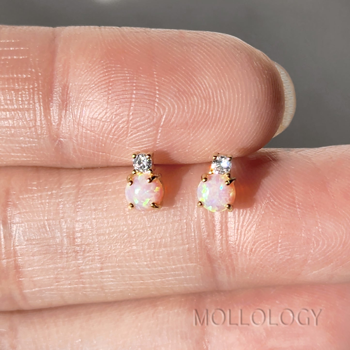 Opal earrings with diamond accents on a finger, brand 'Mollology' visible