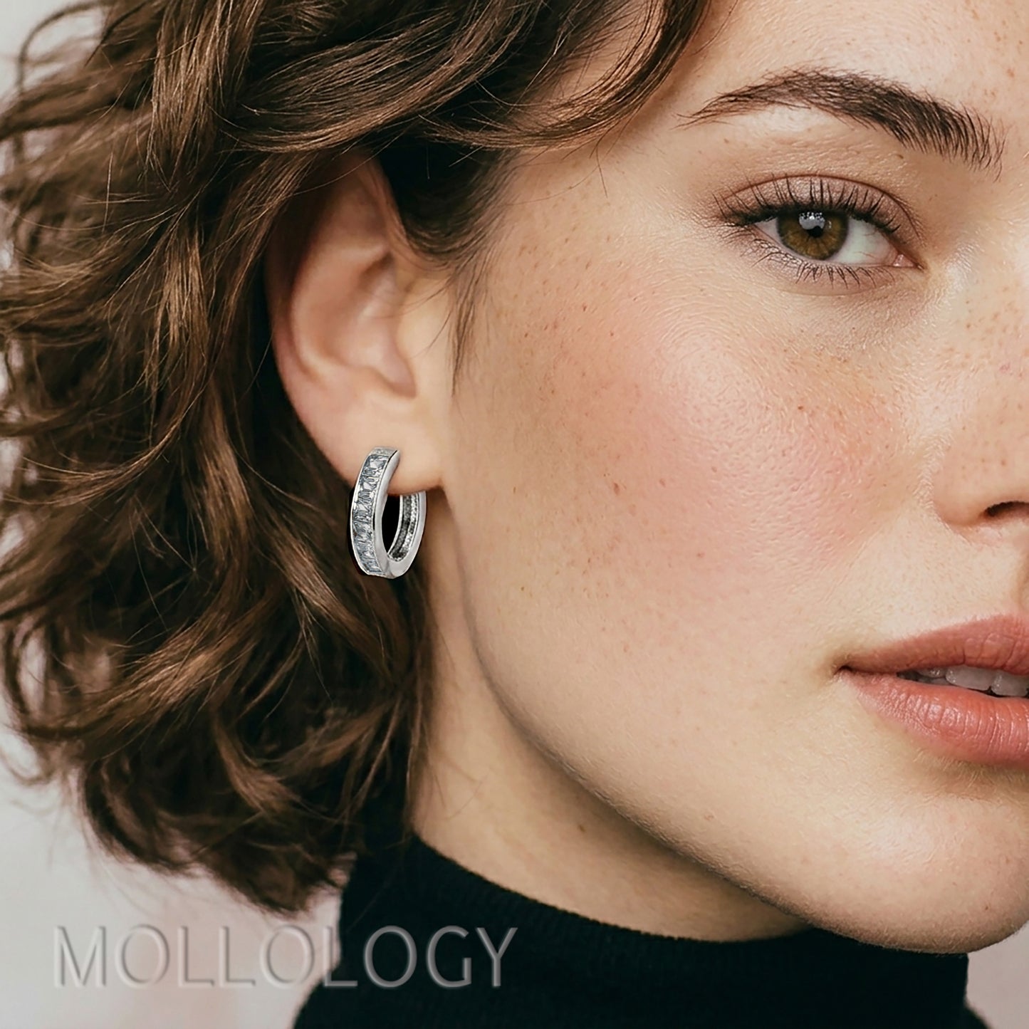 Close-up of a woman wearing a silver hoop earring with 'Mollology' branding.