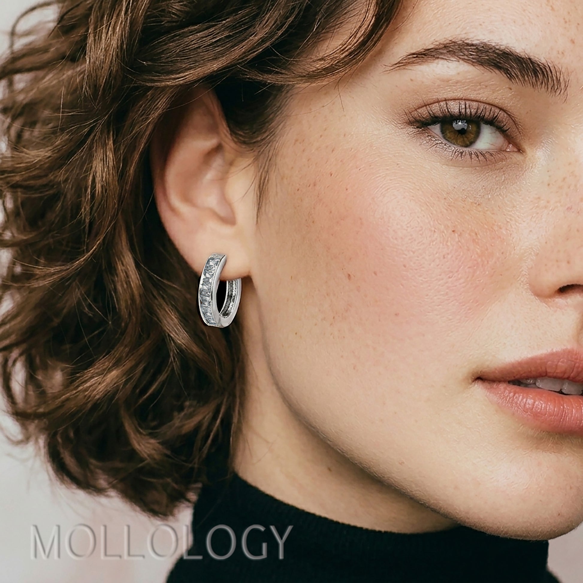 Close-up of a woman wearing a silver hoop earring with 'Mollology' branding.