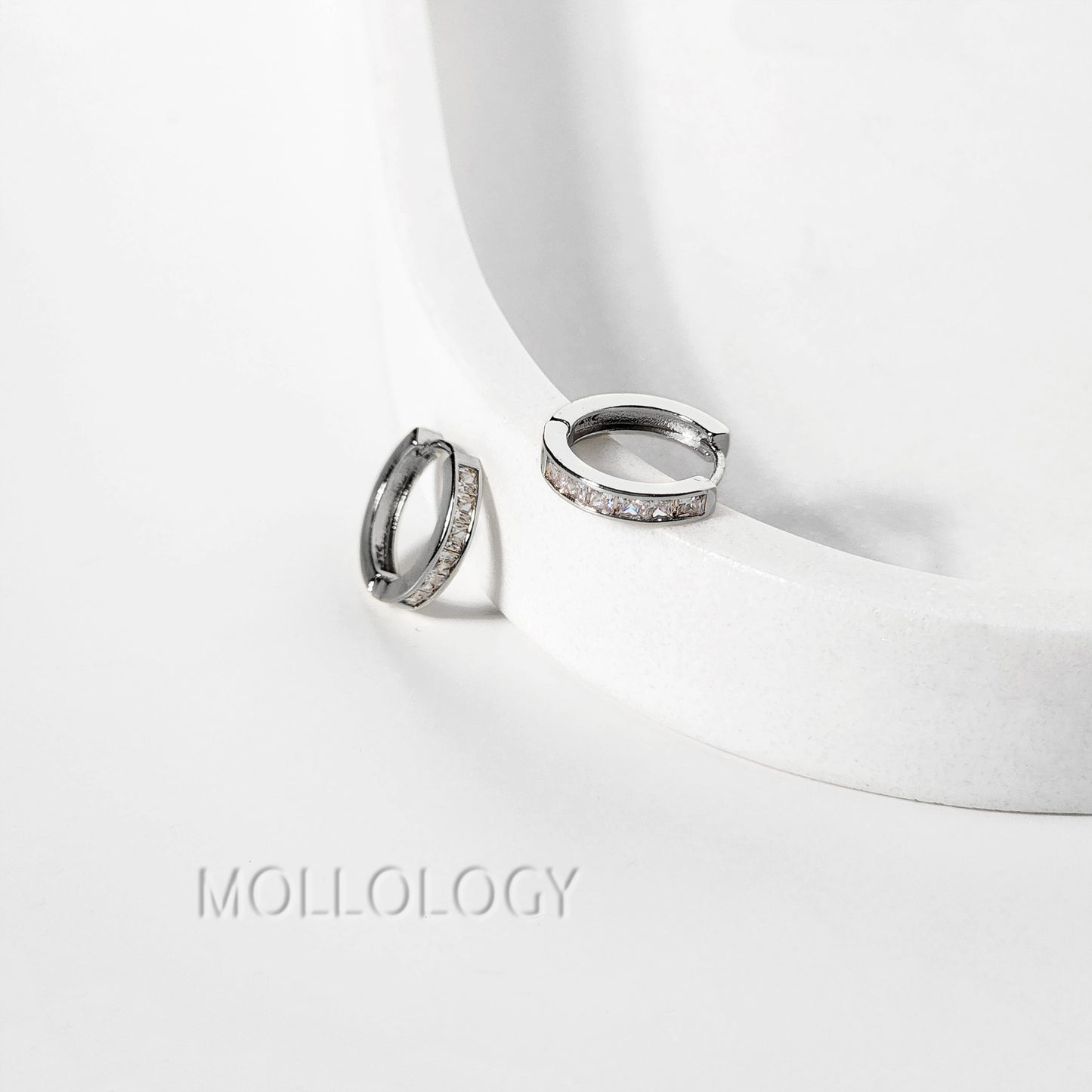 Silver diamond hoop earrings on a white surface with 'Mollology' branding.