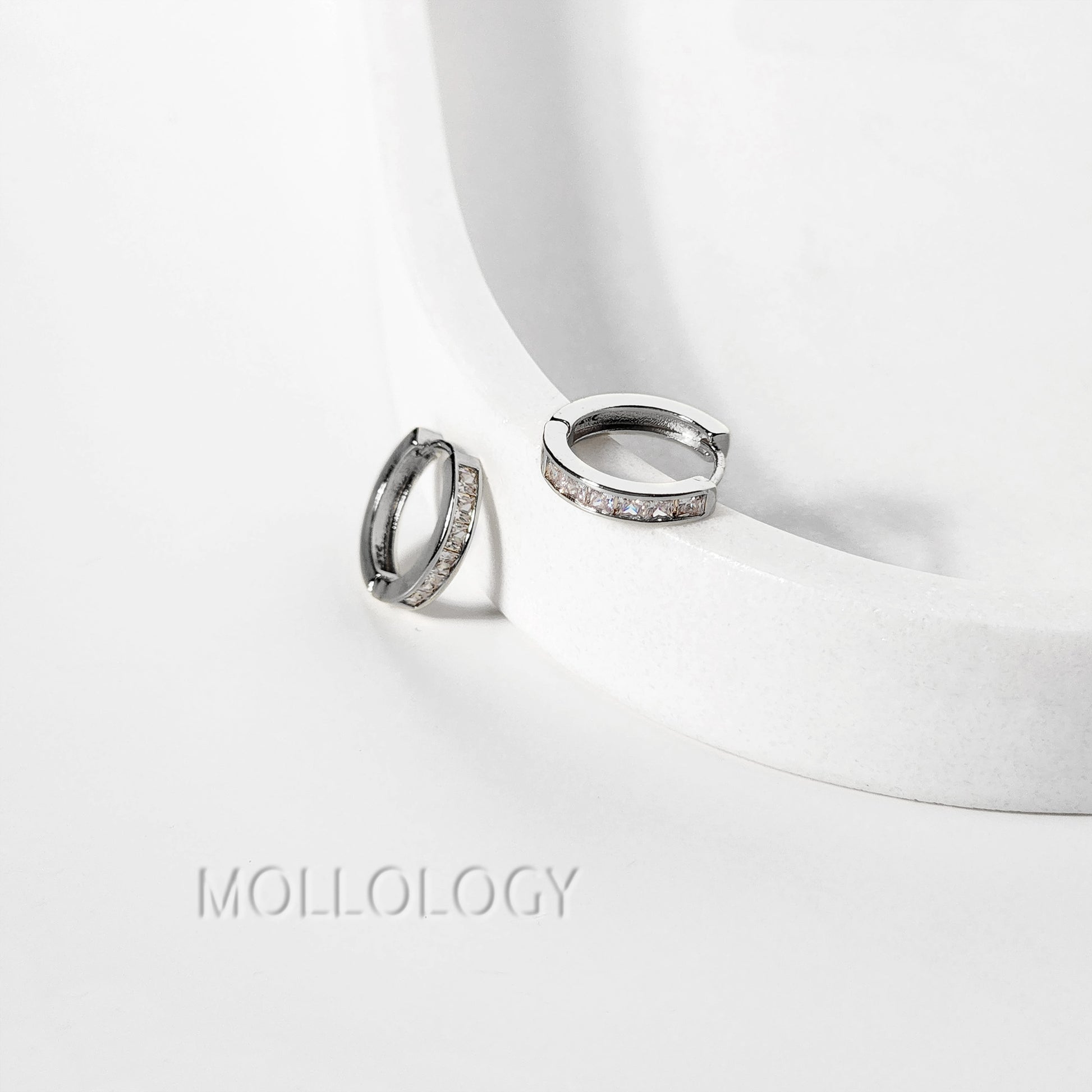 Silver diamond hoop earrings on a white surface with 'Mollology' branding.