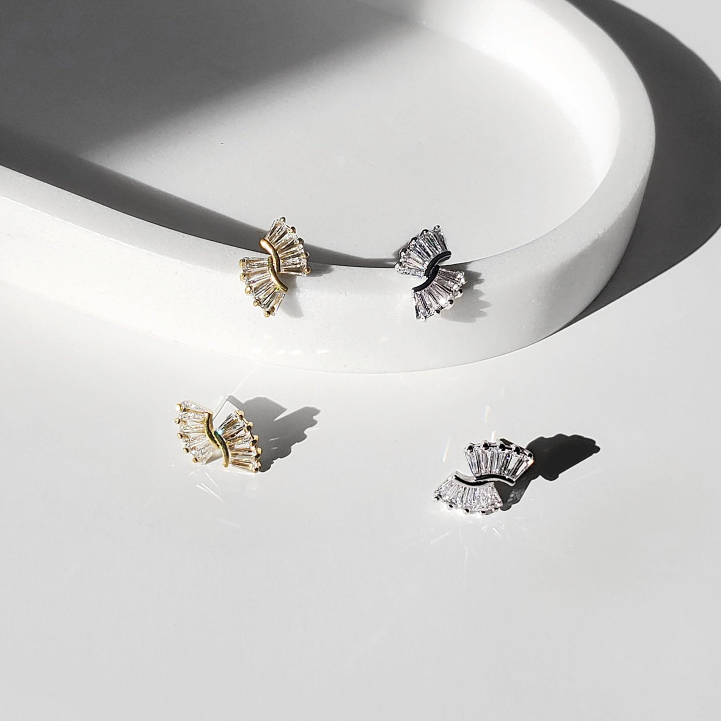 Gold and silver art deco baguette fan stud earrings shown close-up in a bright studio setting.