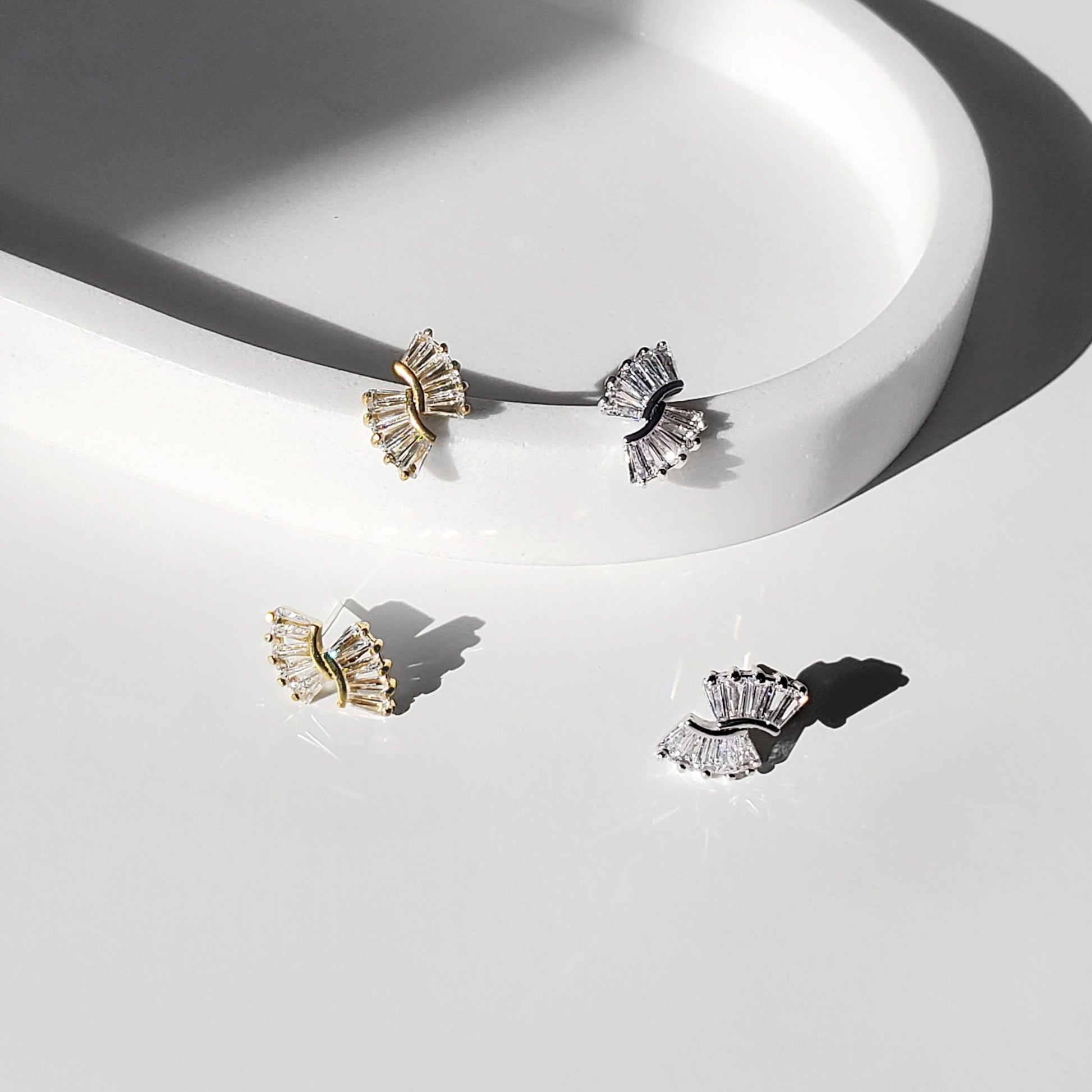 Gold and silver art deco baguette fan stud earrings shown close-up in a bright studio setting.
