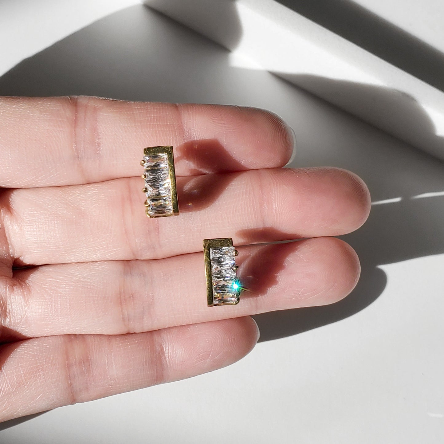 These dainty stud earrings feature a unique curved baguette bar that hugs the ear, giving the look of huggie hoops in a comfortable stud style. The sleek Art Deco–inspired design in gold or silver makes them perfect for minimalist everyday wear, as well as chic wedding jewelry for brides and bridesmaids.