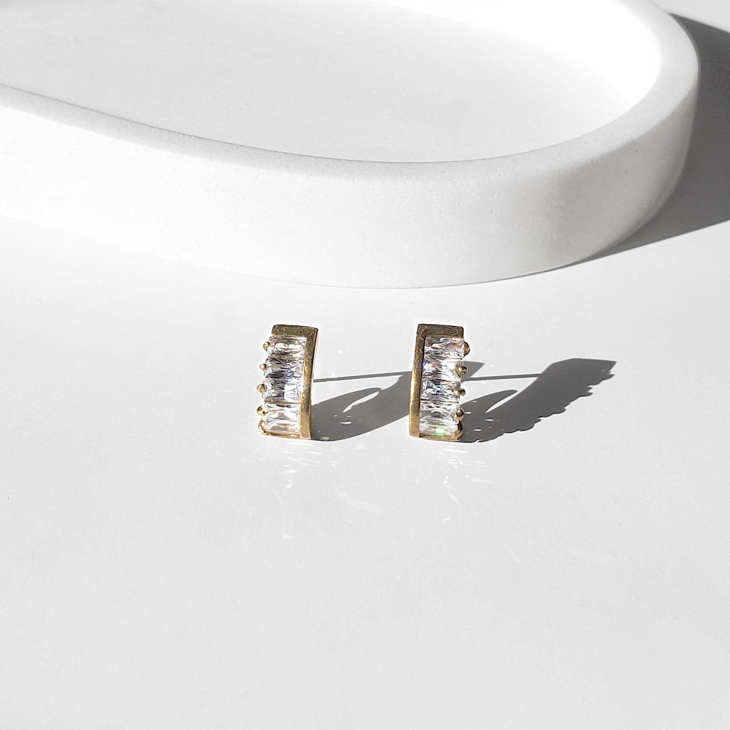 These dainty stud earrings feature a unique curved baguette bar that hugs the ear, giving the look of huggie hoops in a comfortable stud style. The sleek Art Deco–inspired design in gold or silver makes them perfect for minimalist everyday wear, as well as chic wedding jewelry for brides and bridesmaids.