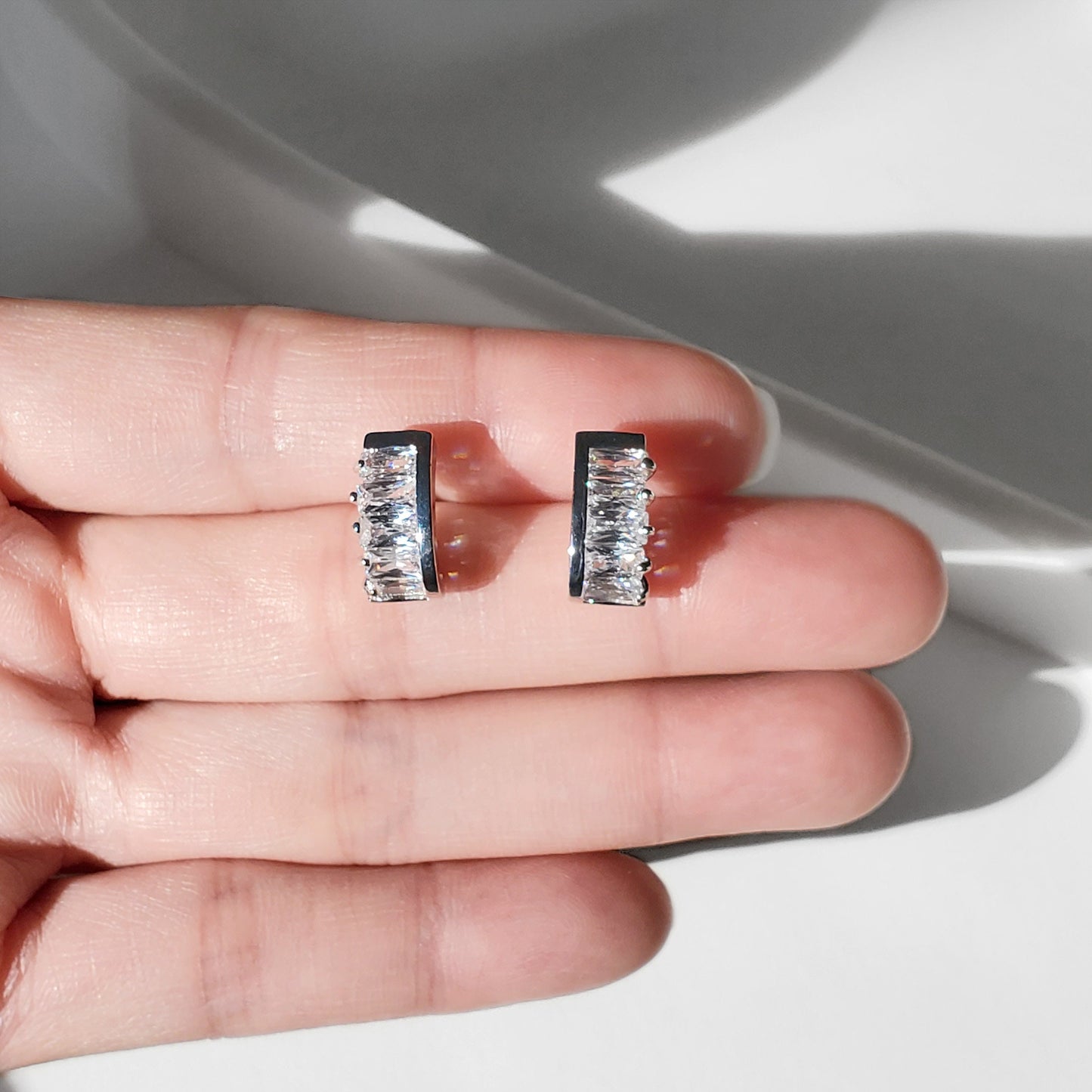 These dainty stud earrings feature a unique curved baguette bar that hugs the ear, giving the look of huggie hoops in a comfortable stud style. The sleek Art Deco–inspired design in gold or silver makes them perfect for minimalist everyday wear, as well as chic wedding jewelry for brides and bridesmaids.