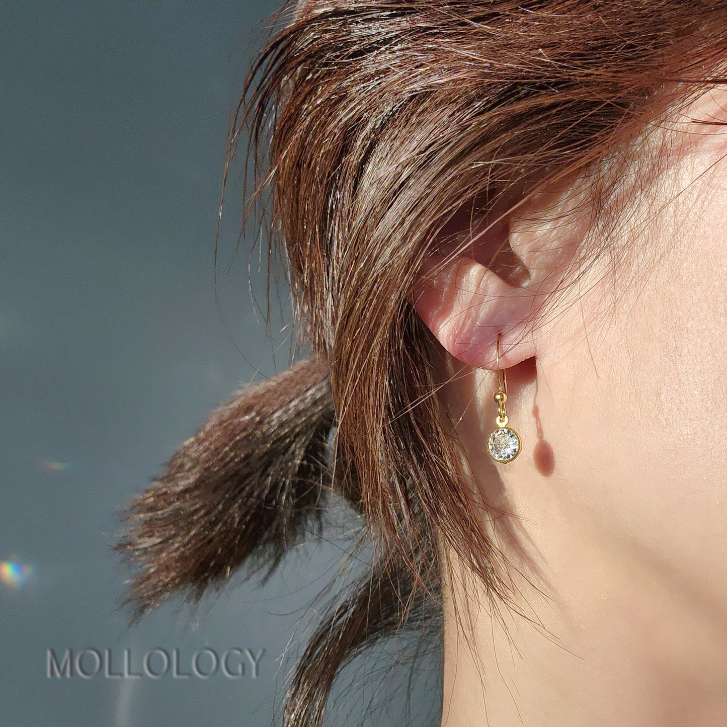 Dainty gold bezel CZ drop earrings on ear, minimalist everyday dangle studs in sunlight