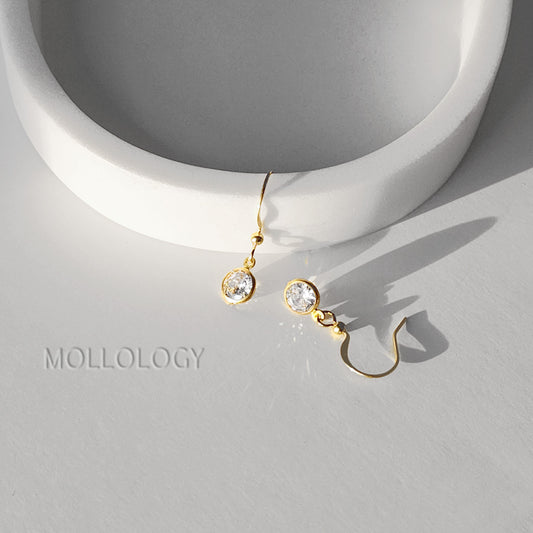 Gold bezel CZ drop earrings on white dish, delicate minimalist dangle earrings casting soft shadows