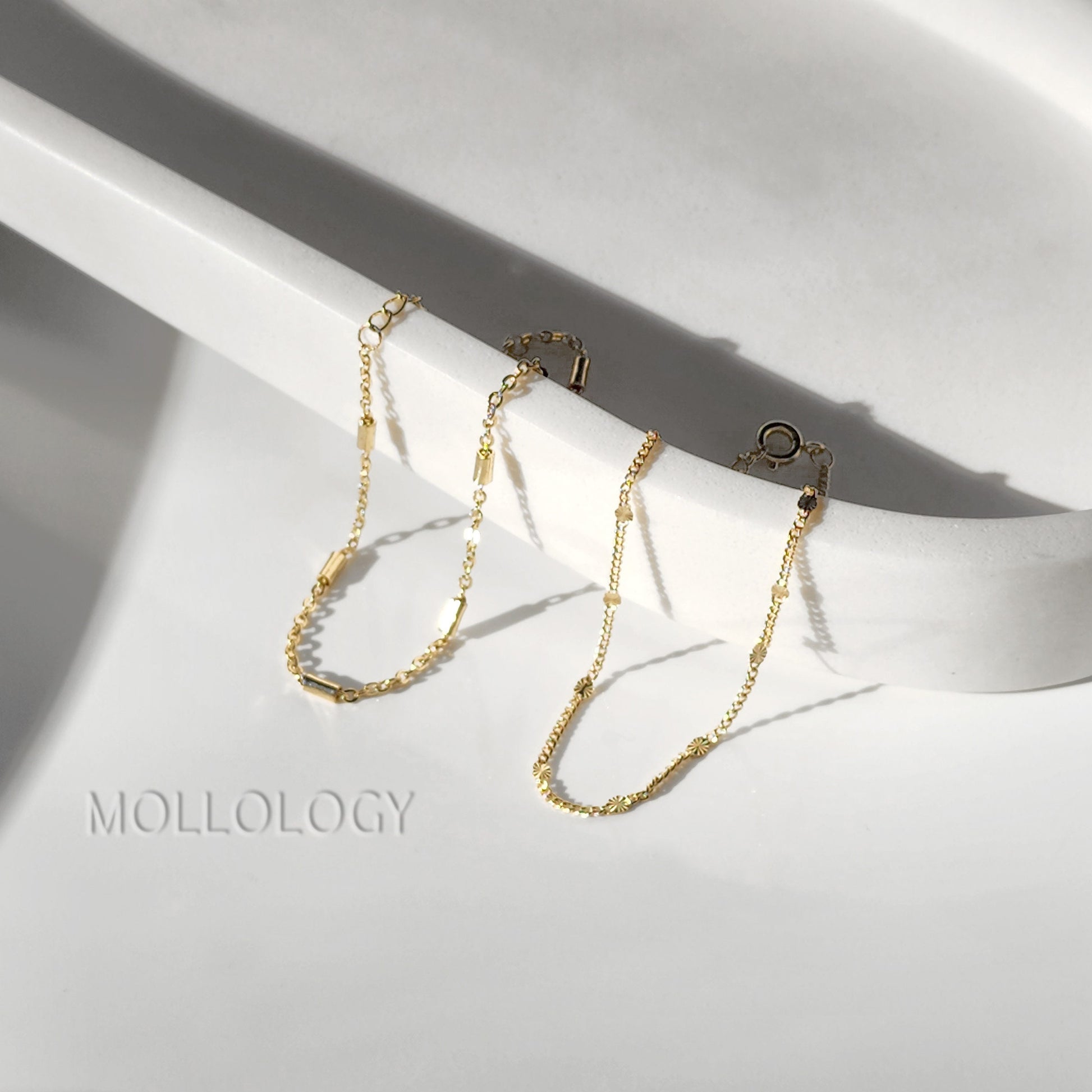 Three delicate gold-plated layering bracelets displayed on a white stand, highlighting the different chain textures and adjustable extension.