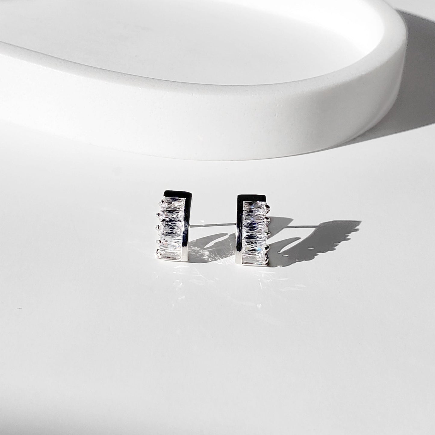 These dainty stud earrings feature a unique curved baguette bar that hugs the ear, giving the look of huggie hoops in a comfortable stud style. The sleek Art Deco–inspired design in gold or silver makes them perfect for minimalist everyday wear, as well as chic wedding jewelry for brides and bridesmaids.