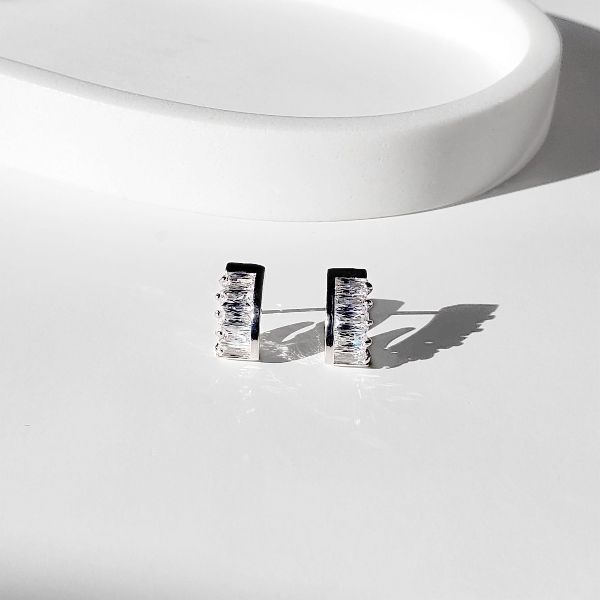 These dainty stud earrings feature a unique curved baguette bar that hugs the ear, giving the look of huggie hoops in a comfortable stud style. The sleek Art Deco–inspired design in gold or silver makes them perfect for minimalist everyday wear, as well as chic wedding jewelry for brides and bridesmaids.