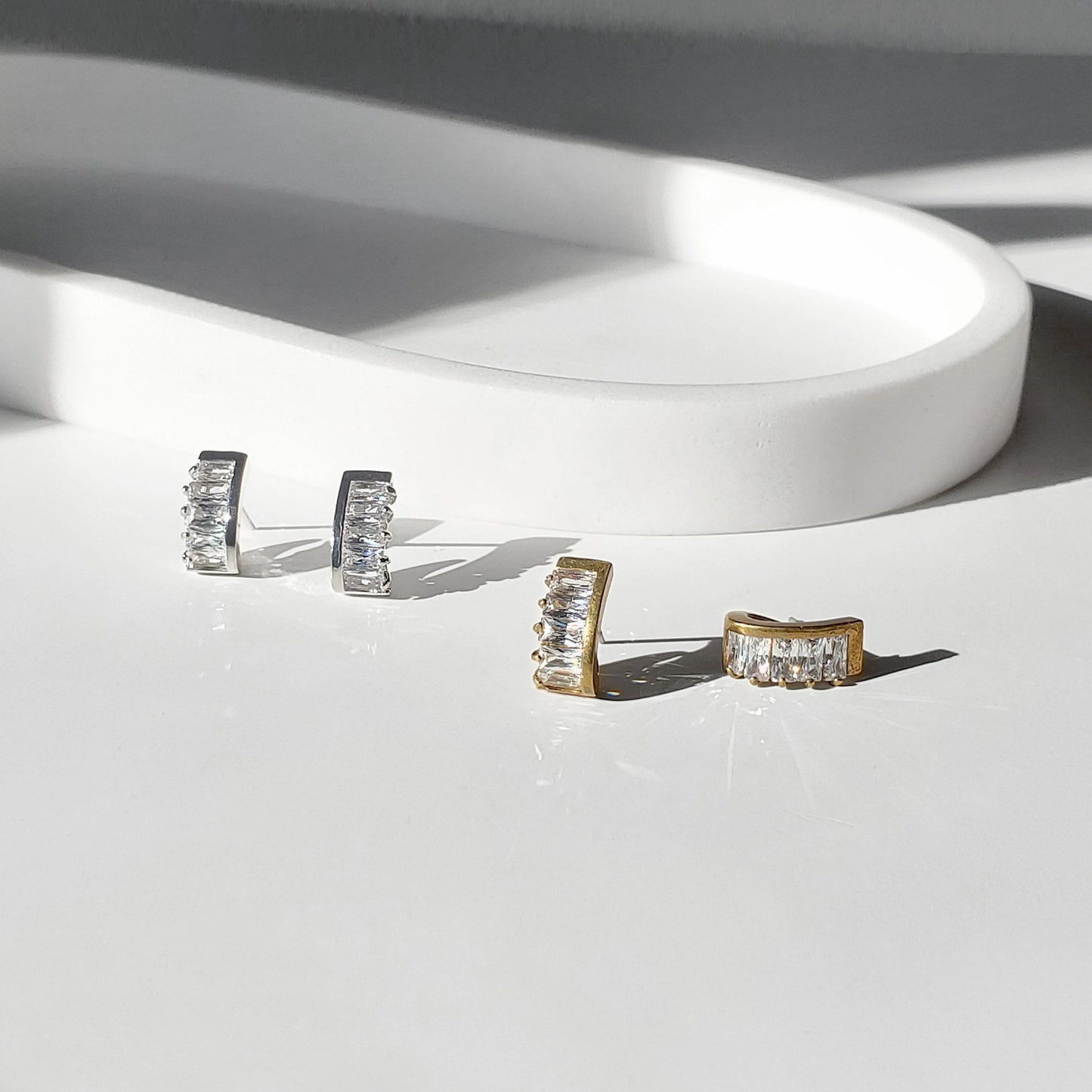 These dainty stud earrings feature a unique curved baguette bar that hugs the ear, giving the look of huggie hoops in a comfortable stud style. The sleek Art Deco–inspired design in gold or silver makes them perfect for minimalist everyday wear, as well as chic wedding jewelry for brides and bridesmaids.