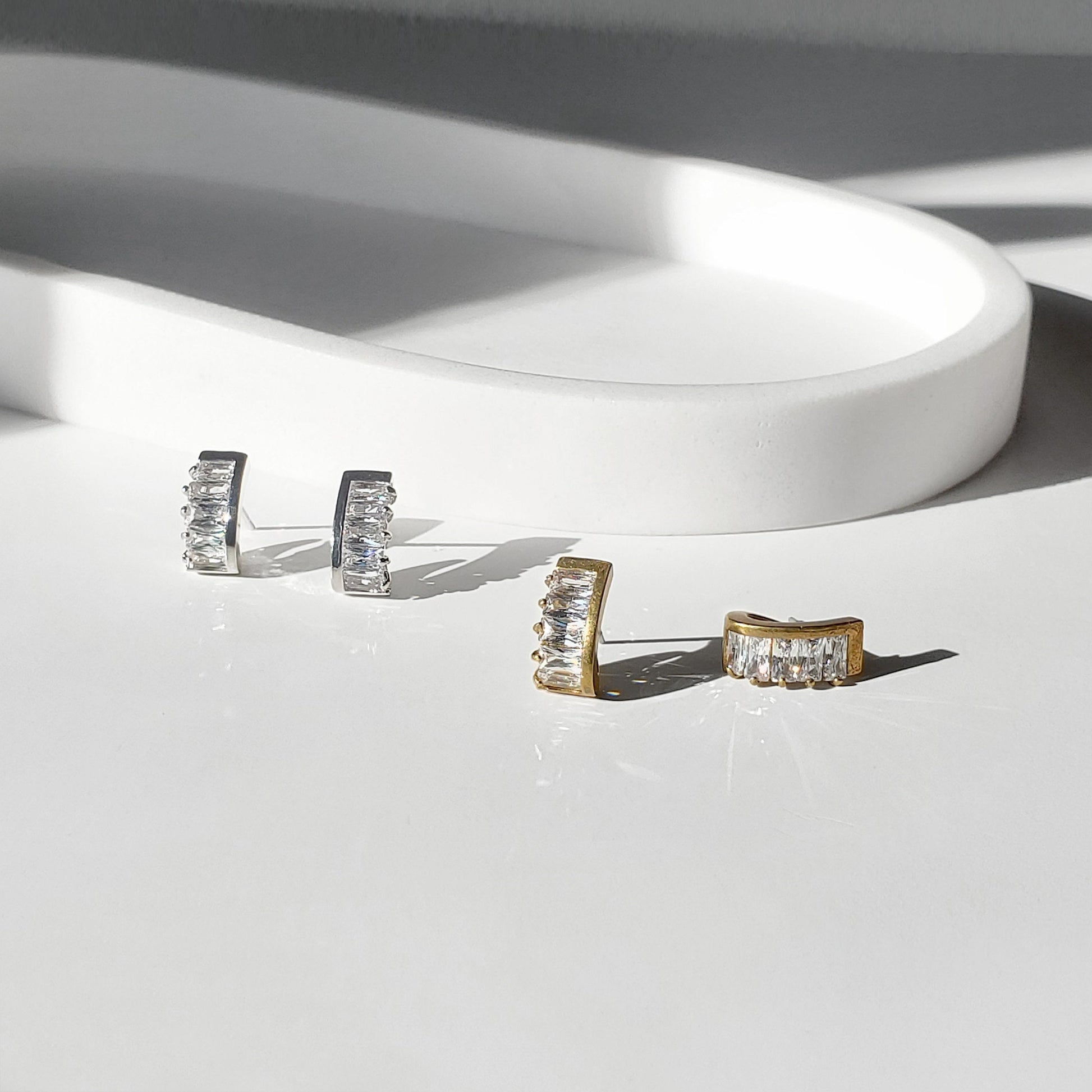 These dainty stud earrings feature a unique curved baguette bar that hugs the ear, giving the look of huggie hoops in a comfortable stud style. The sleek Art Deco–inspired design in gold or silver makes them perfect for minimalist everyday wear, as well as chic wedding jewelry for brides and bridesmaids.