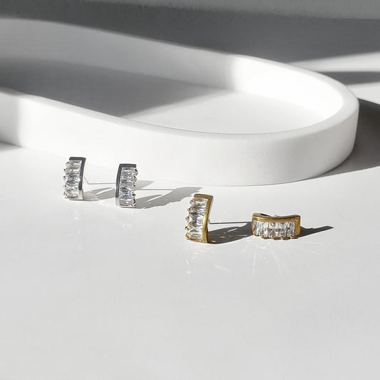 These dainty stud earrings feature a unique curved baguette bar that hugs the ear, giving the look of huggie hoops in a comfortable stud style. The sleek Art Deco–inspired design in gold or silver makes them perfect for minimalist everyday wear, as well as chic wedding jewelry for brides and bridesmaids.