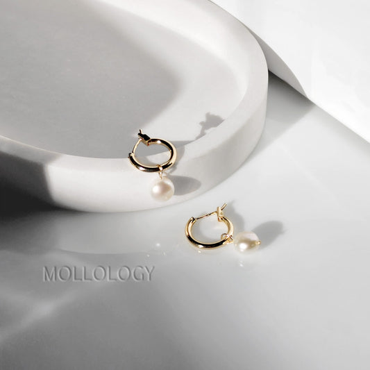 These Freshwater Pearl Huggies feature lustrous natural pearls on dainty gold huggie hoops, creating an elegant yet minimalist look that works for every day. Perfect as everyday pearl earrings or for dressing up, these lightweight hoops are ideal for layering with other earrings and make a beautiful gift for her.