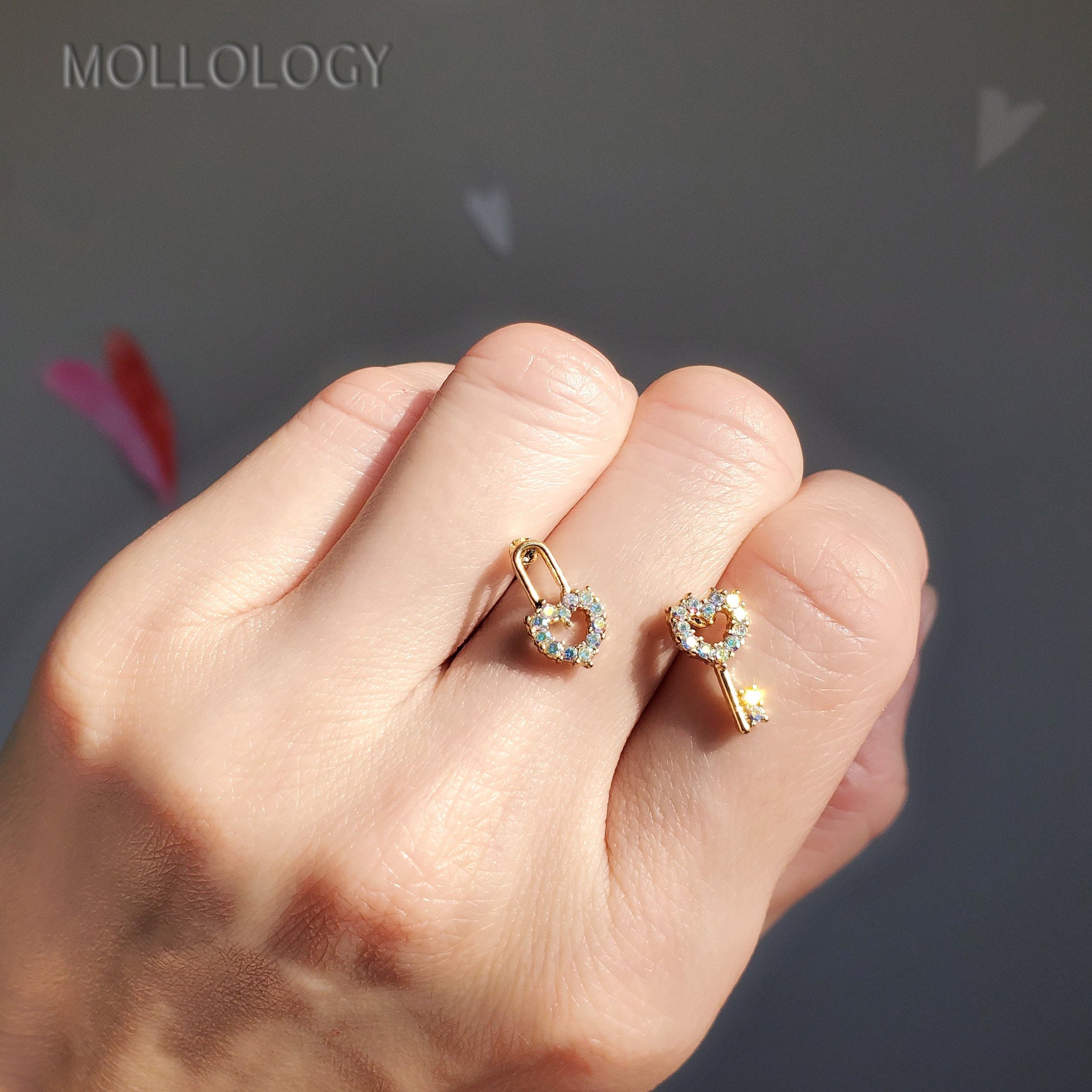 A person's hand holding a pair of iridescent heart-shaped earrings with a gold finish and silver posts.
