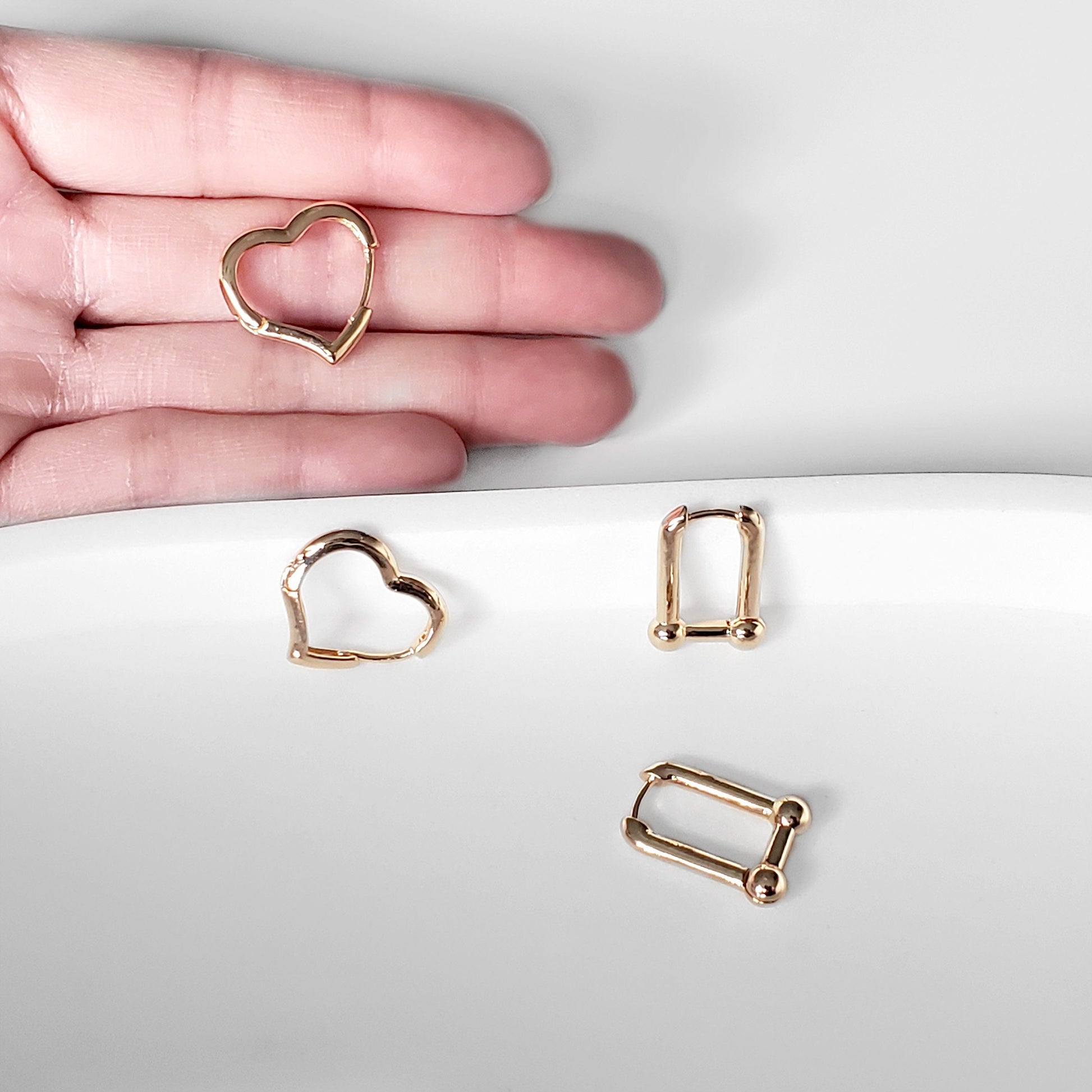 A set of gold-colored hoop earrings in various sizes, designed in the shape of hearts, displayed on a white surface.