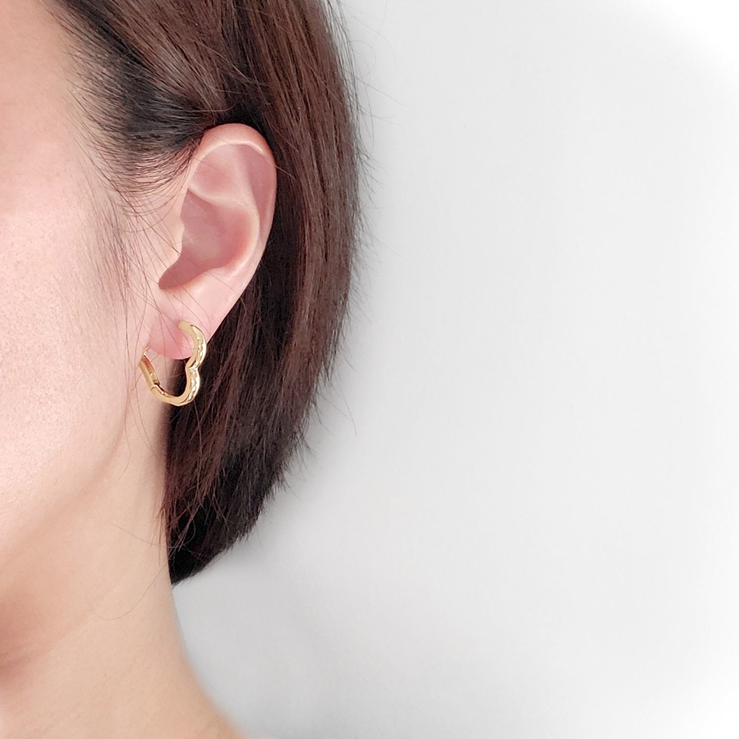 A set of gold-colored hoop earrings in various sizes, designed in the shape of hearts, displayed on a white surface.
