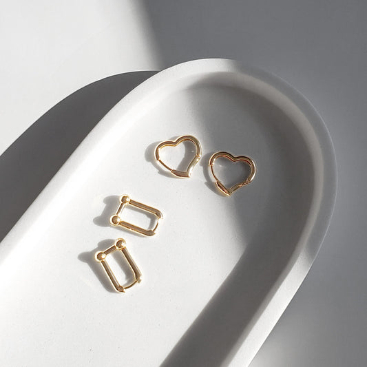 A set of gold-colored hoop earrings in various sizes, designed in the shape of hearts, displayed on a white surface.