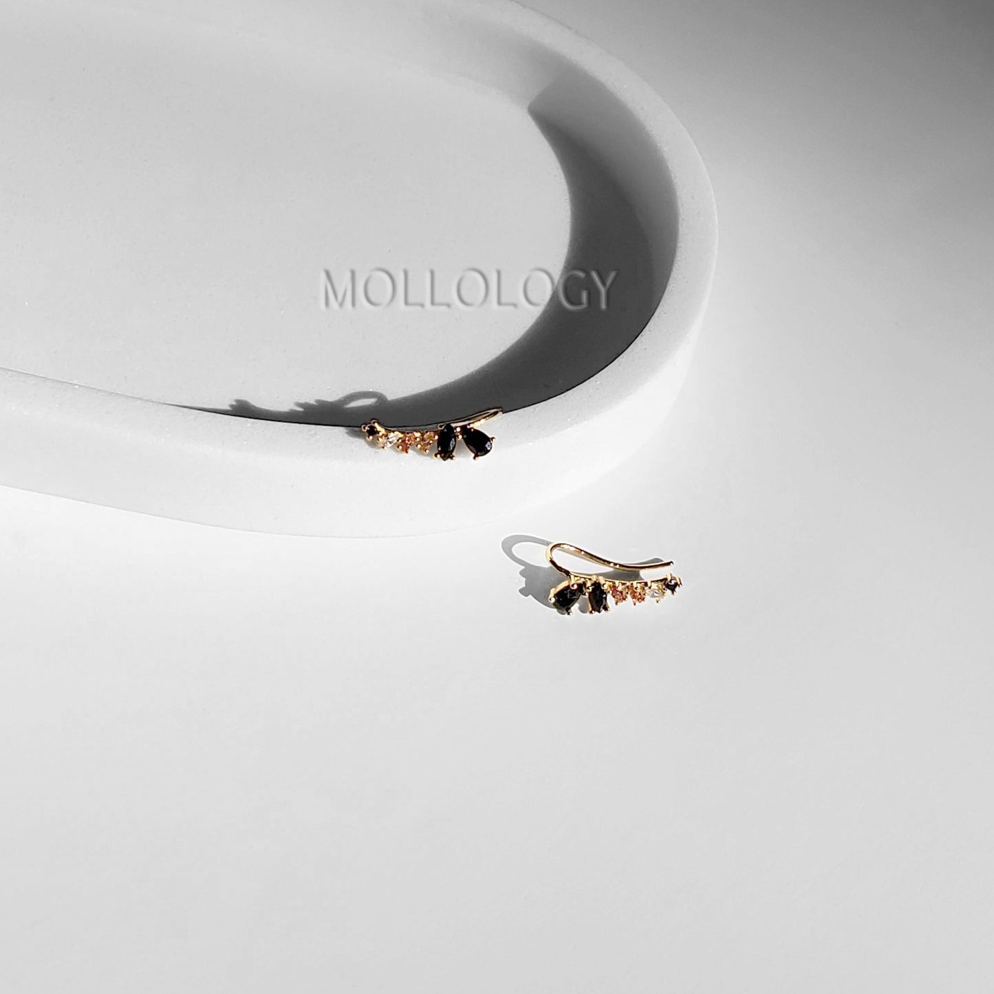 A pair of black onyx and rose quartz ear climbers placed on a white surface with the brand name 'MOLLOLOGY' visible in the background.