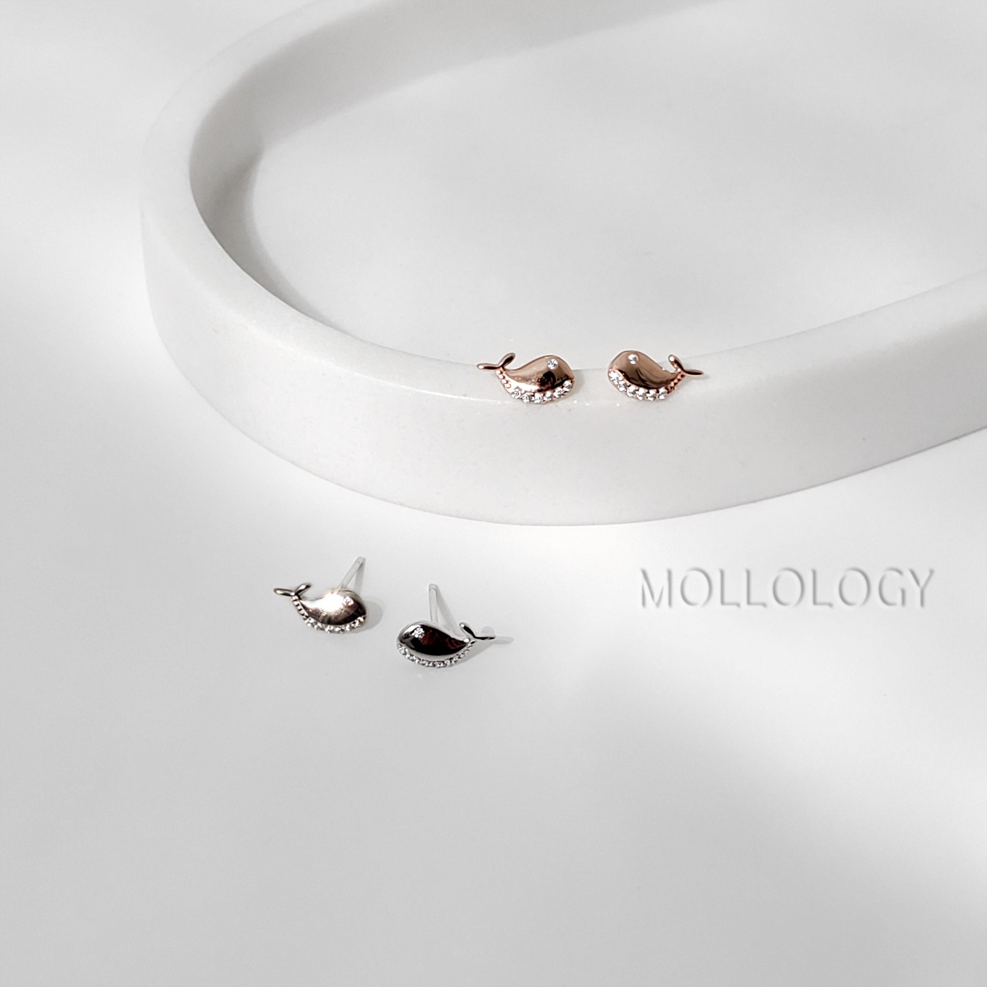 A pair of small, silver stud earrings with rose gold vermeil finish and tiny cubic zirconia embellishments, displayed on a white surface.