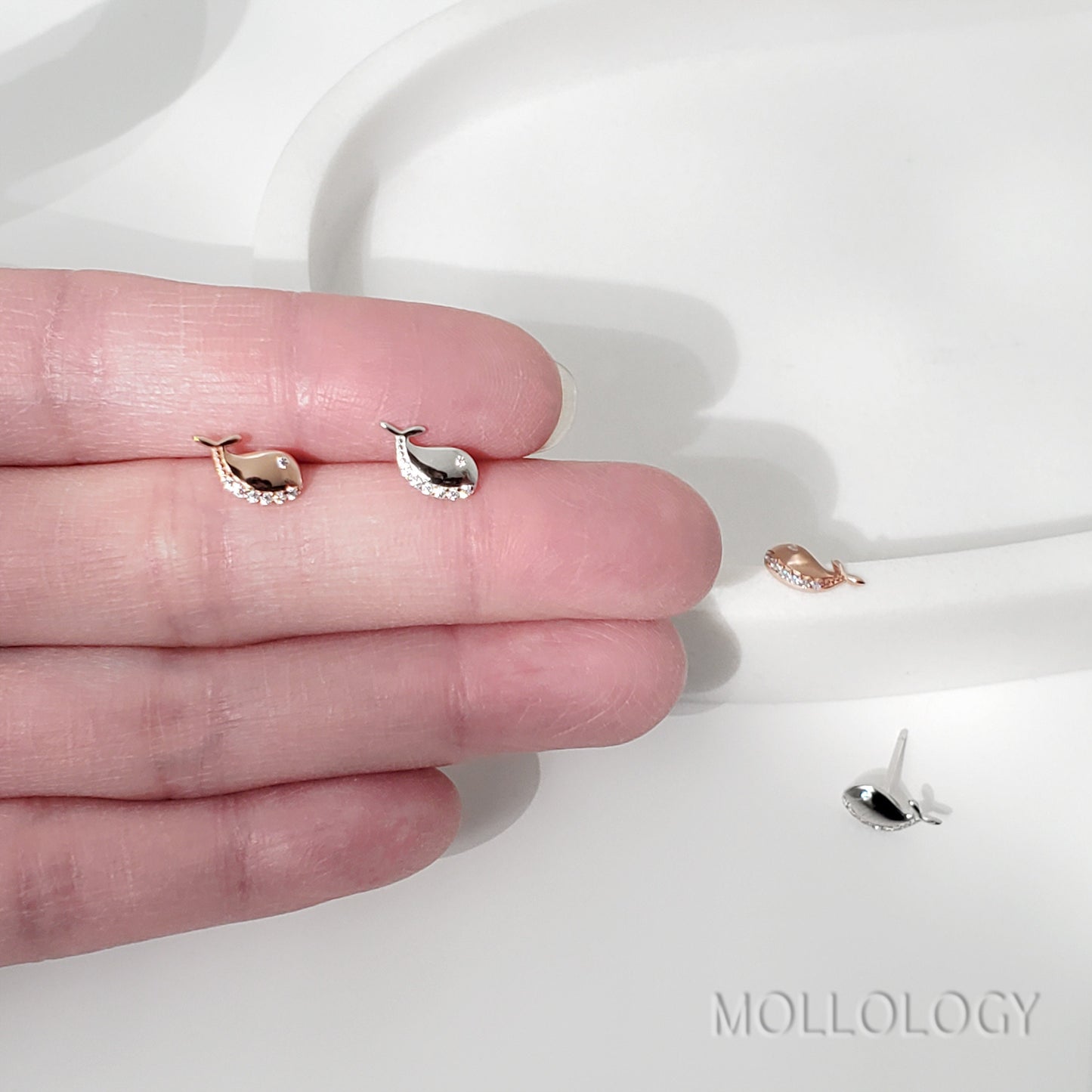 A pair of small, silver stud earrings with rose gold vermeil finish and tiny cubic zirconia embellishments, displayed on a white surface.